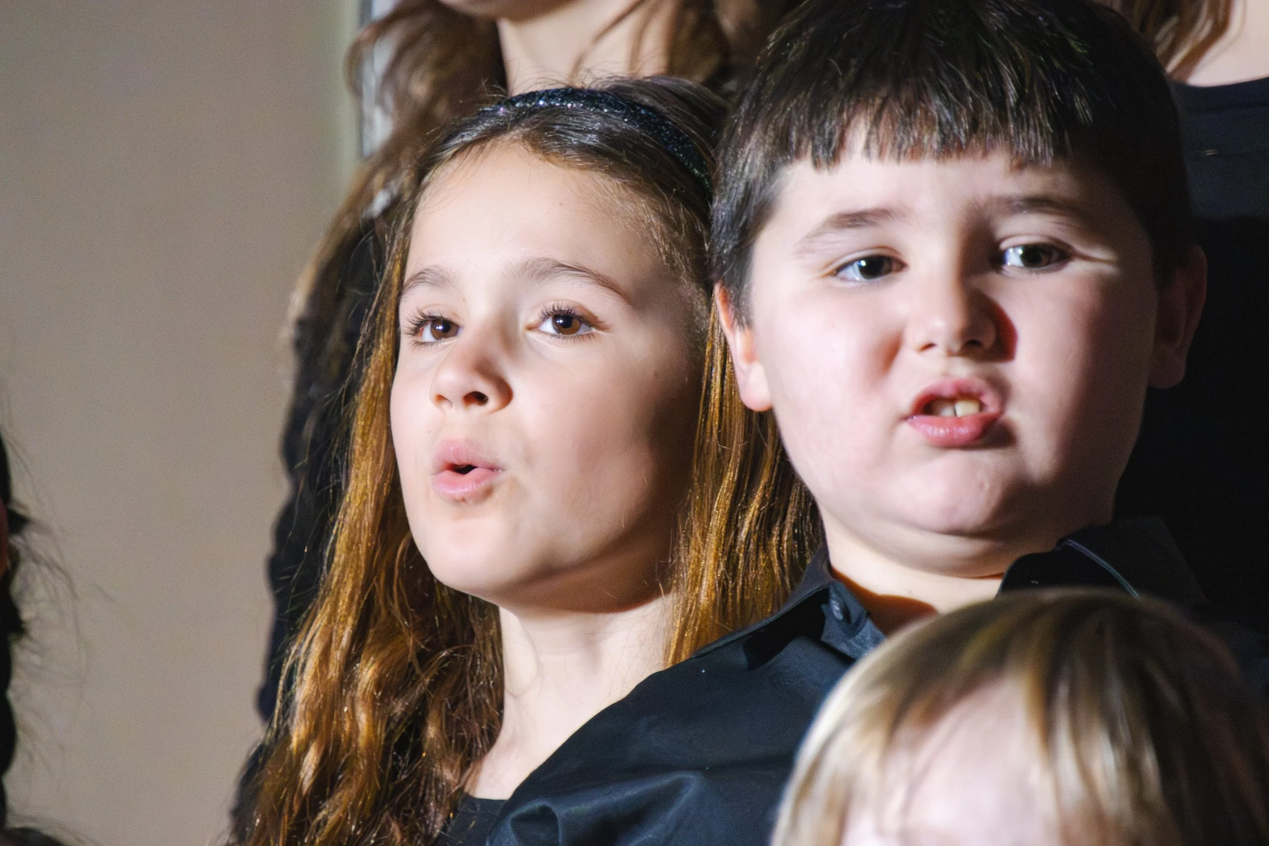 Group of children in black clothing raising their hands during a performance or event, black and white photo.