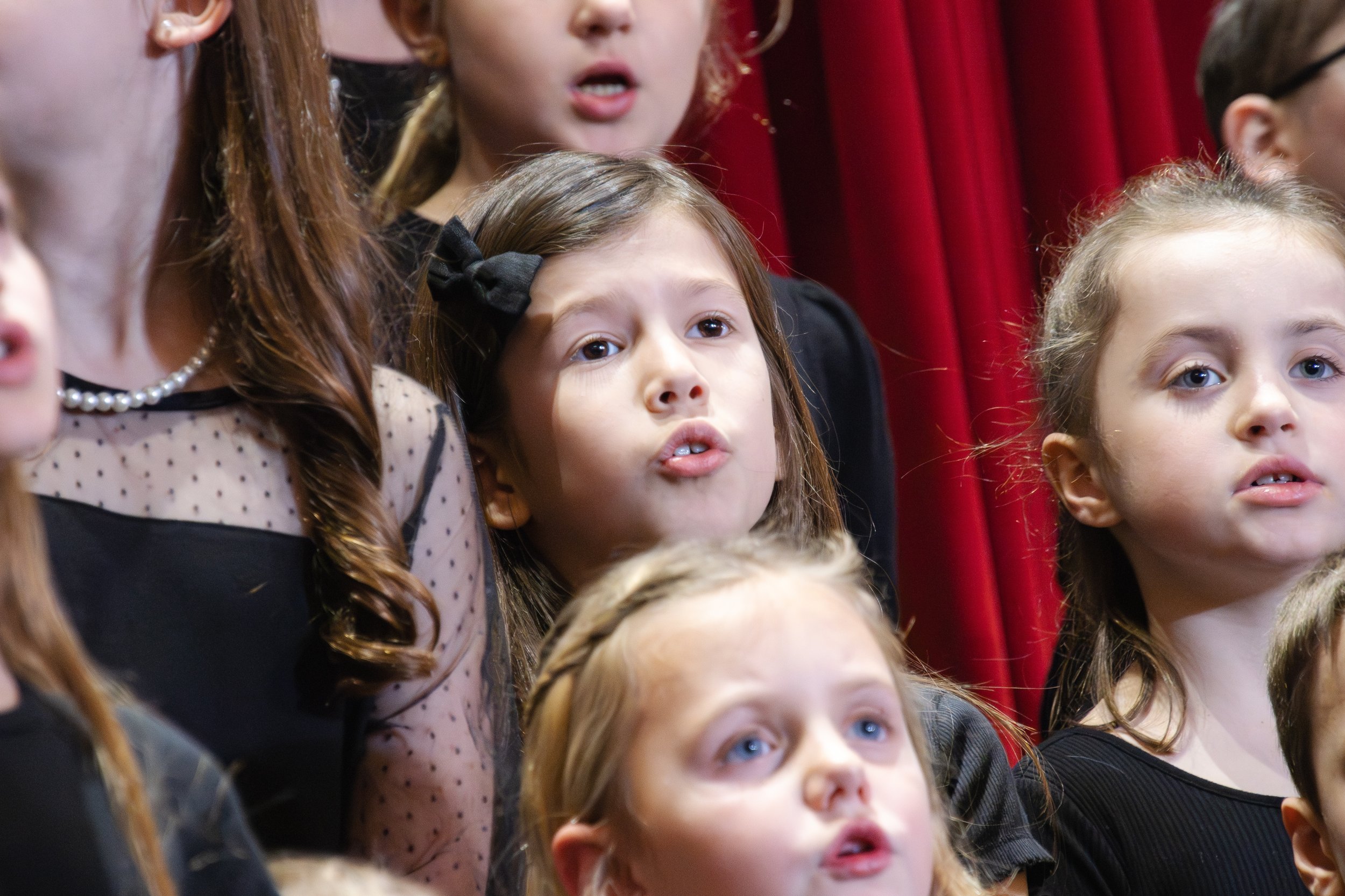 Black and white photo of a group of young girls standing close together, some with serious and attentive expressions, in what appears to be a classroom or event setting.