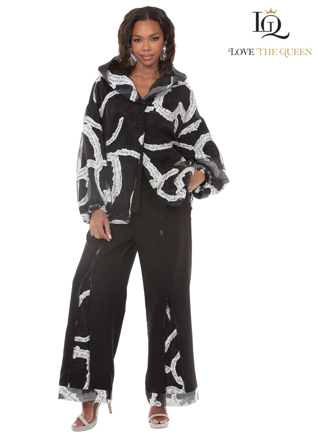 Woman in a black and white patterned hoodie and black pants, standing against a white background, with jewelry and high heels.
