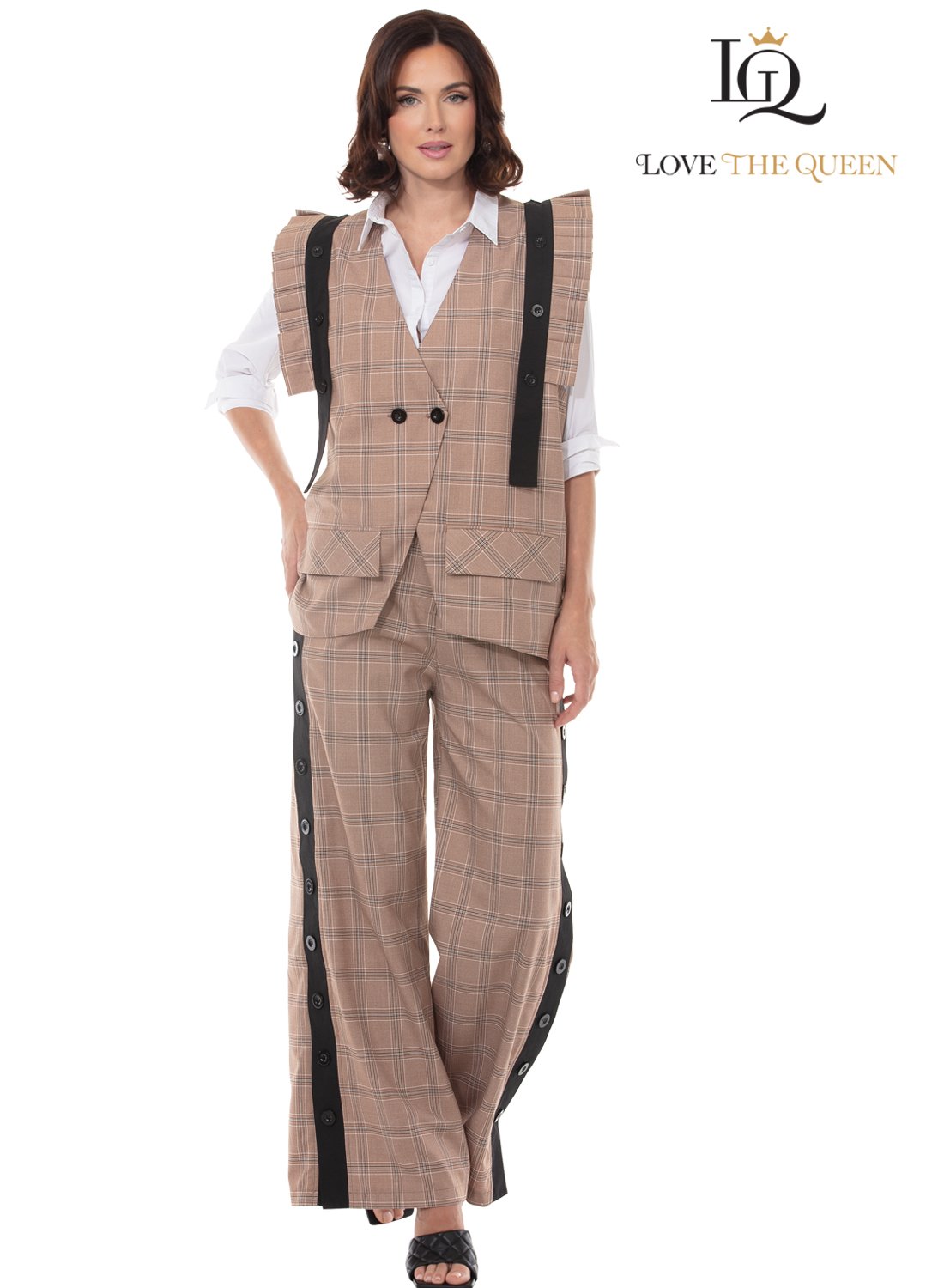 A woman with shoulder-length brown hair wearing a tan plaid vest over a white shirt and matching plaid wide-leg pants with black and gray stripe details and buttons, posing with one hand on her hip against a plain white background. The text reads "Love The Queen" and a logo with a crown and the initials 'TG'.
