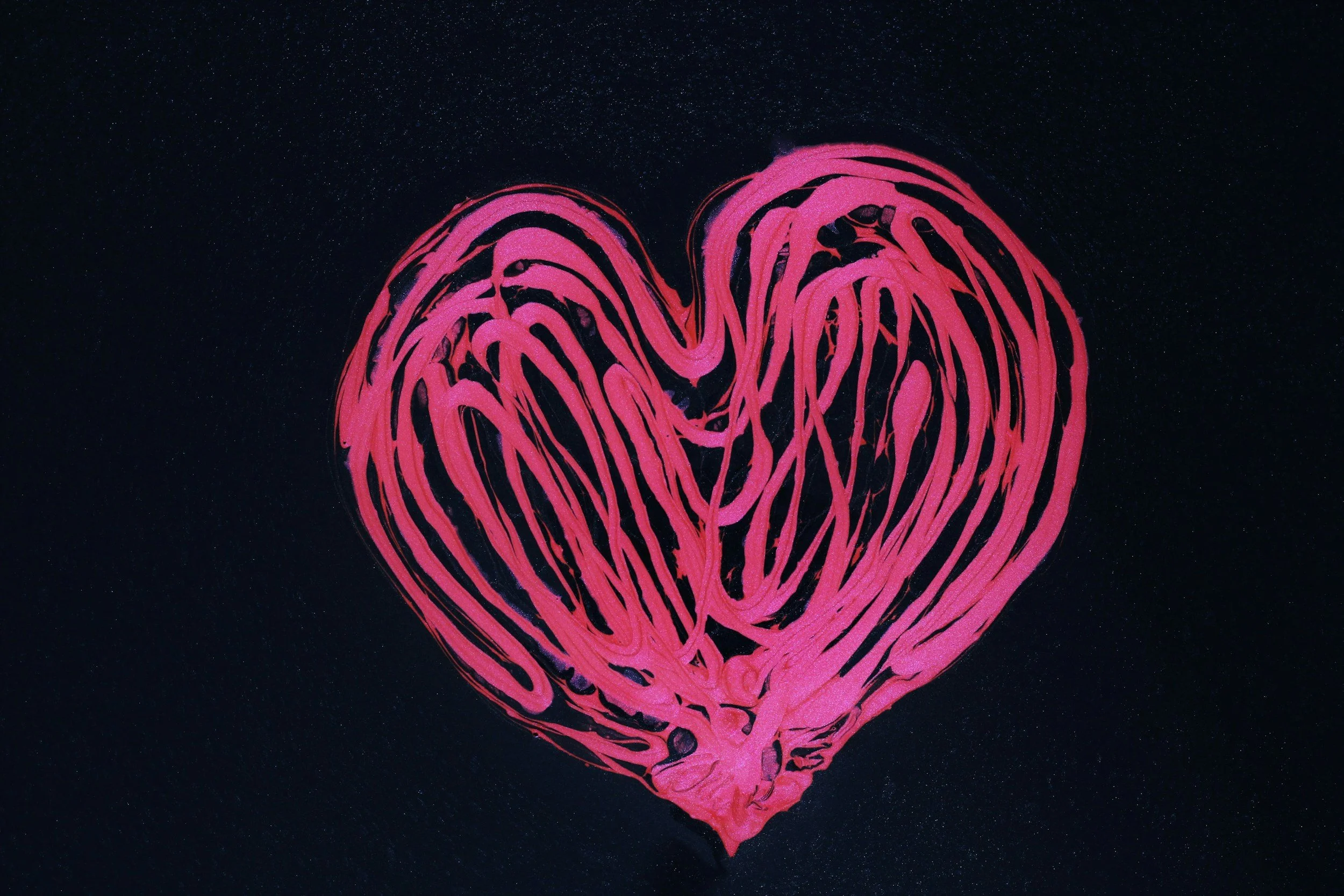 Pink heart-shaped design with swirling patterns on a dark background.