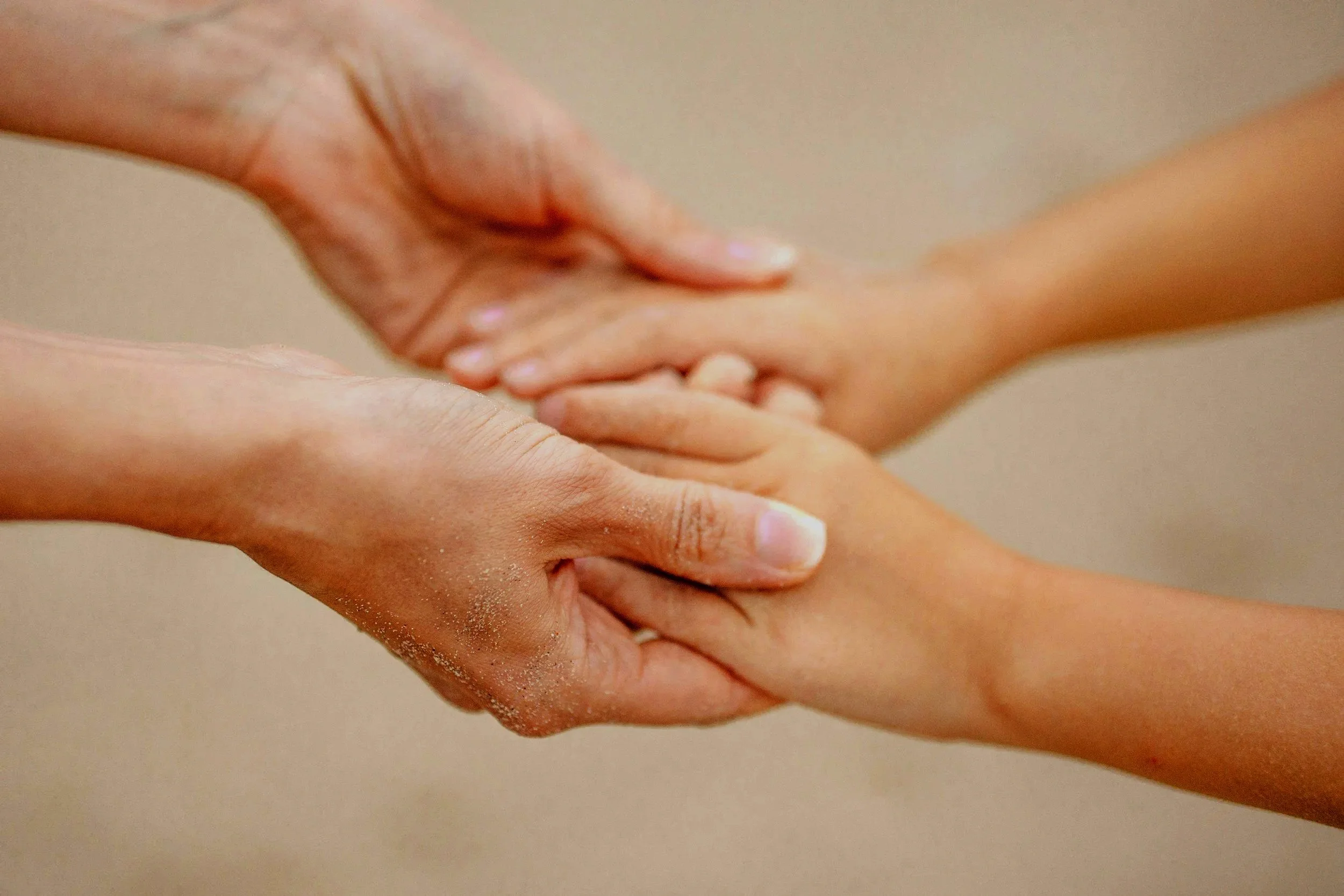 Two pairs of hands holding each other, one appearing older and the other younger.