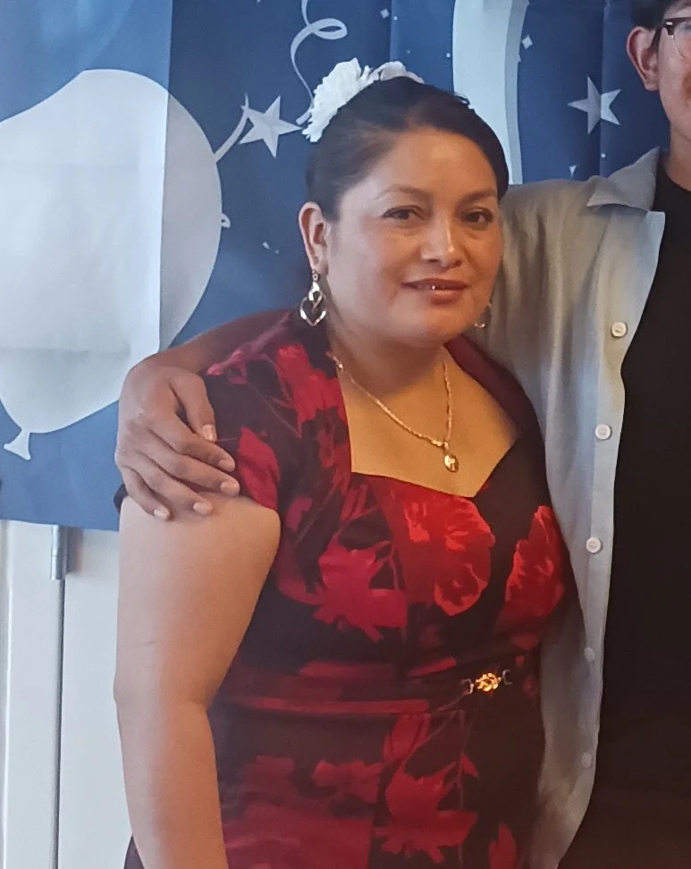 A woman wearing a red and black dress standing, smiling, with someone's arm around her.