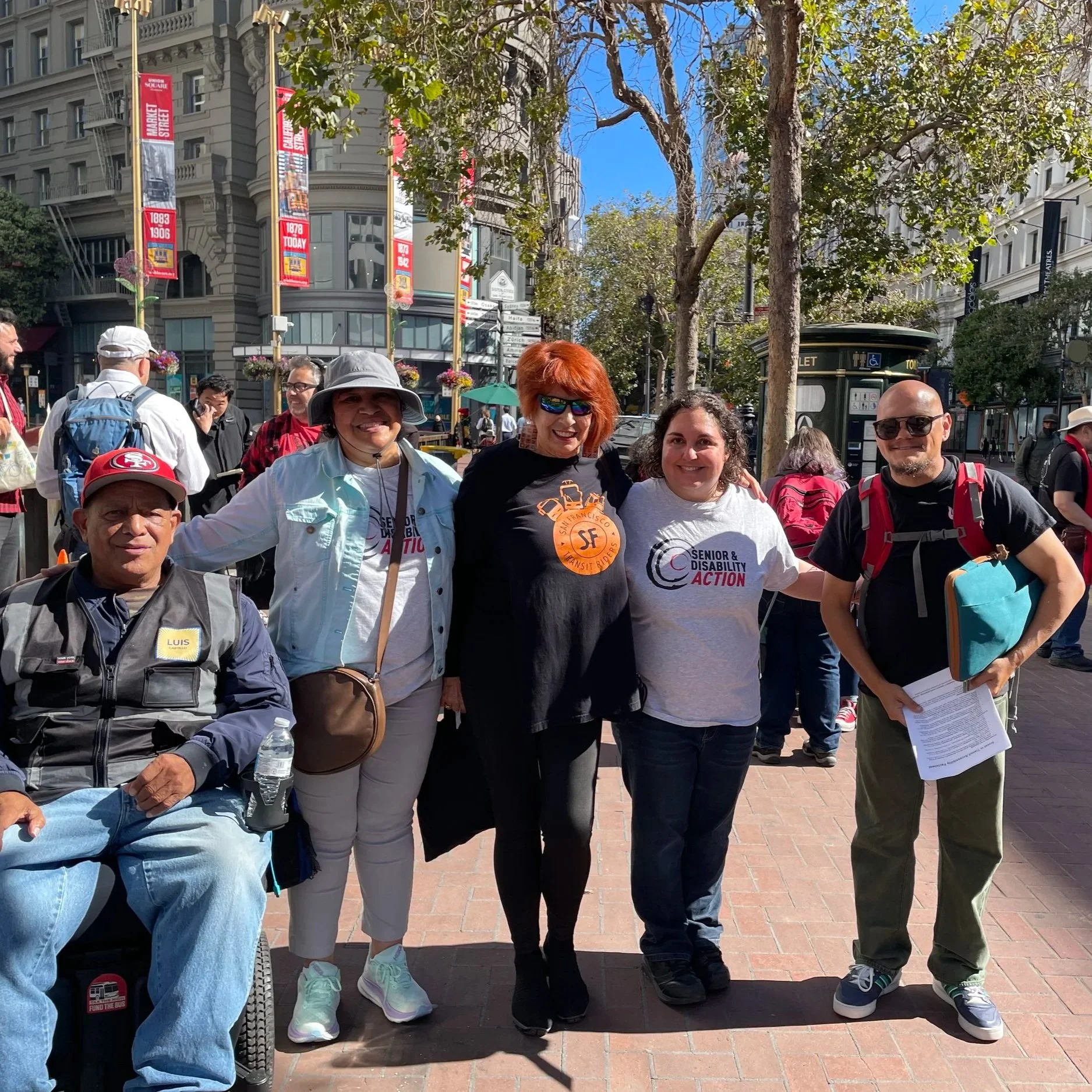 A group of five people outside on Market St wearing shirts for SDA and SF Transit Riders