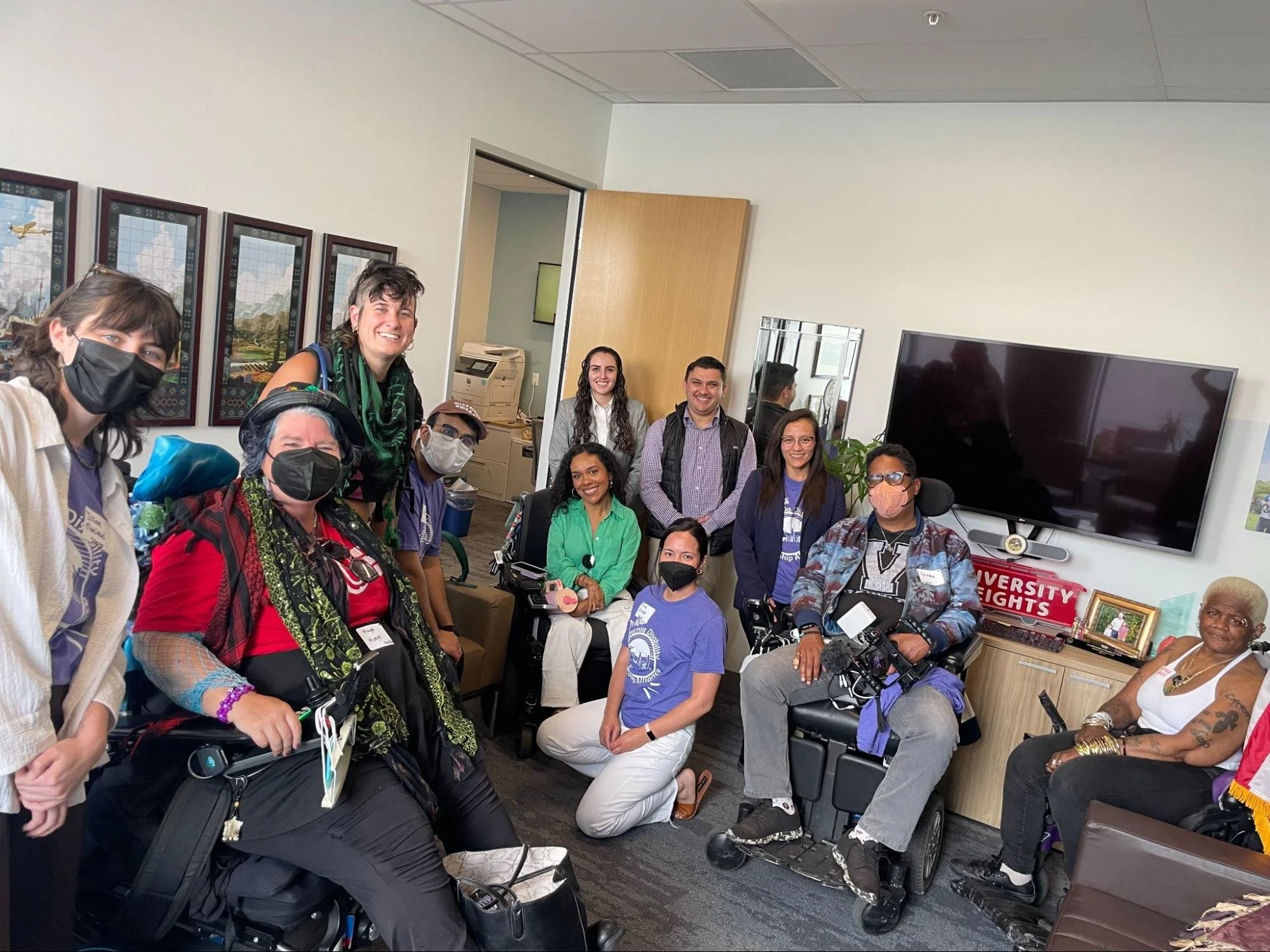 A multiracial group of eleven people, some in wheelchairs and some wearing masks, together in a senate office