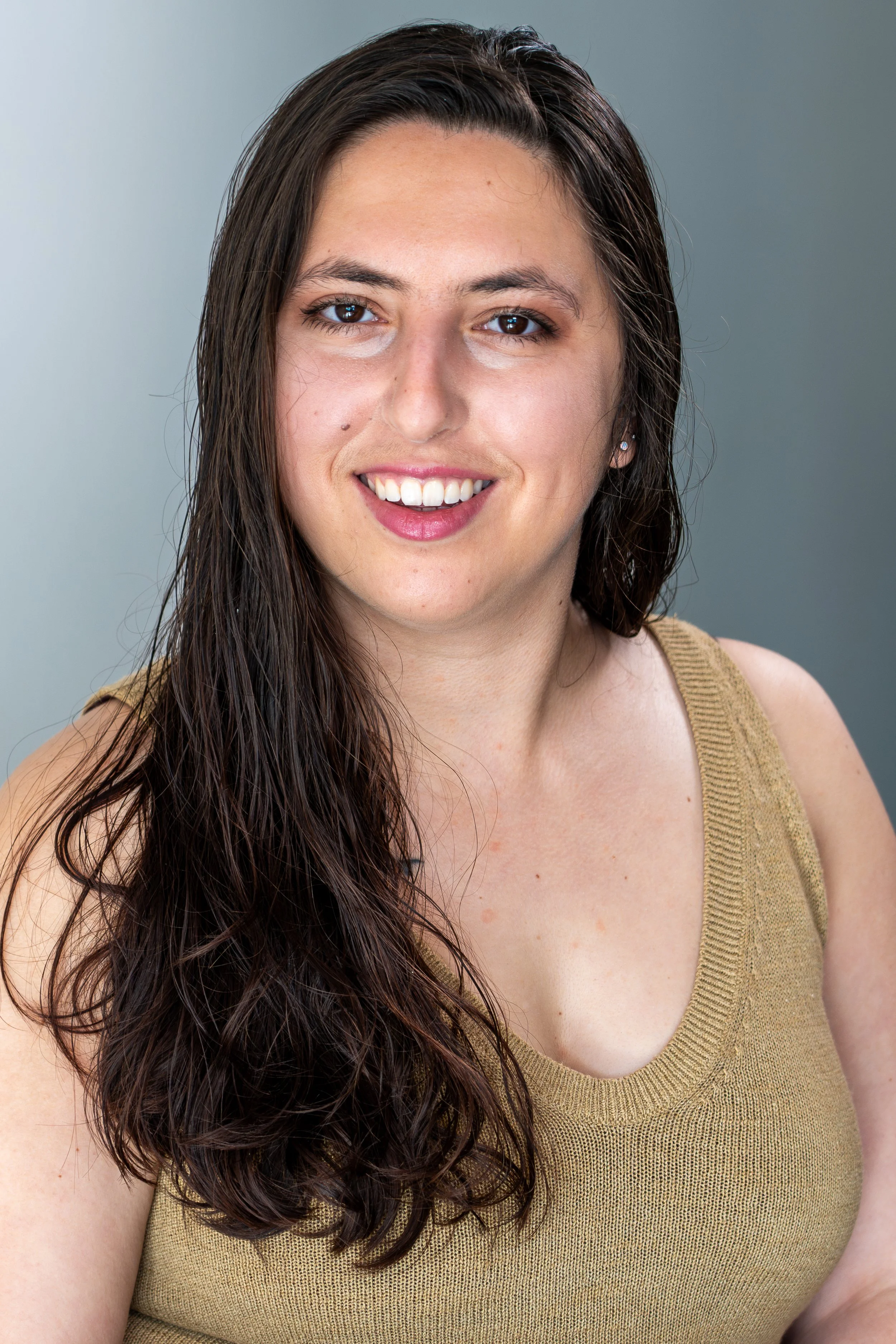 A woman with long brown hair smiling, wearing a brown tank top