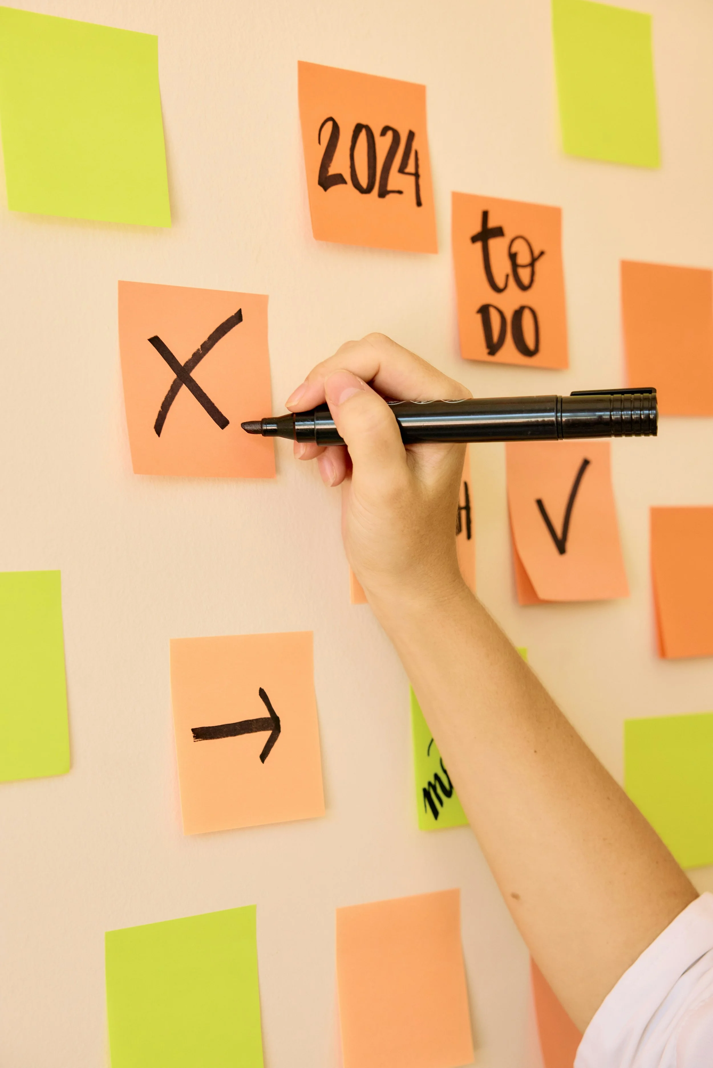 A hand holds a marker writing x's and checks on sticky notes stuck to the wall.