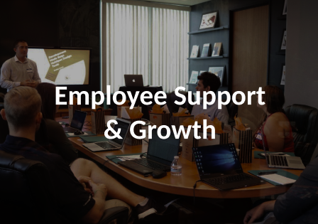 A group of people surrounding a conference table. The manager seems to be at the front presenting to the team. The image is darkened and the words Employee Support and Growth are over it. 