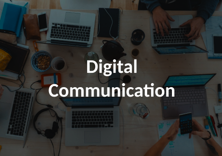 A birds eye view of a conference room table. The table is full of computers, wires, and electronic devices. There are two people typing on some of the computers. The image is darkened with the words Digital Communication over it.