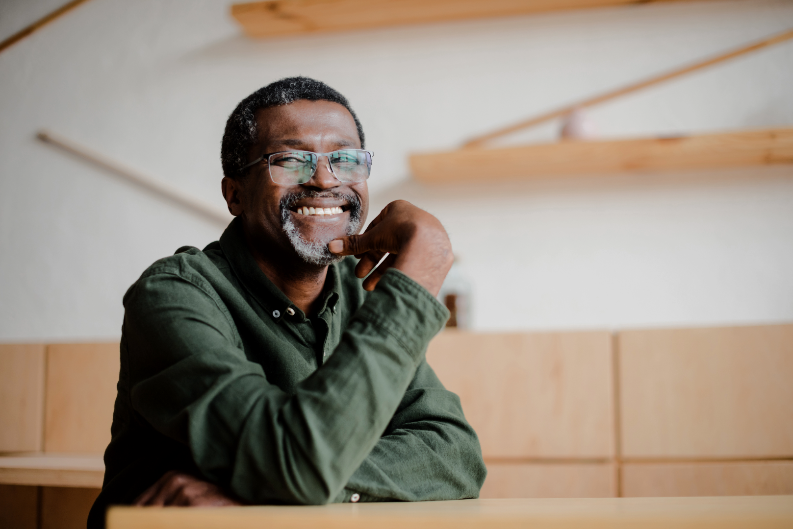 A man sits at a table, smiling with his hand under his chin.