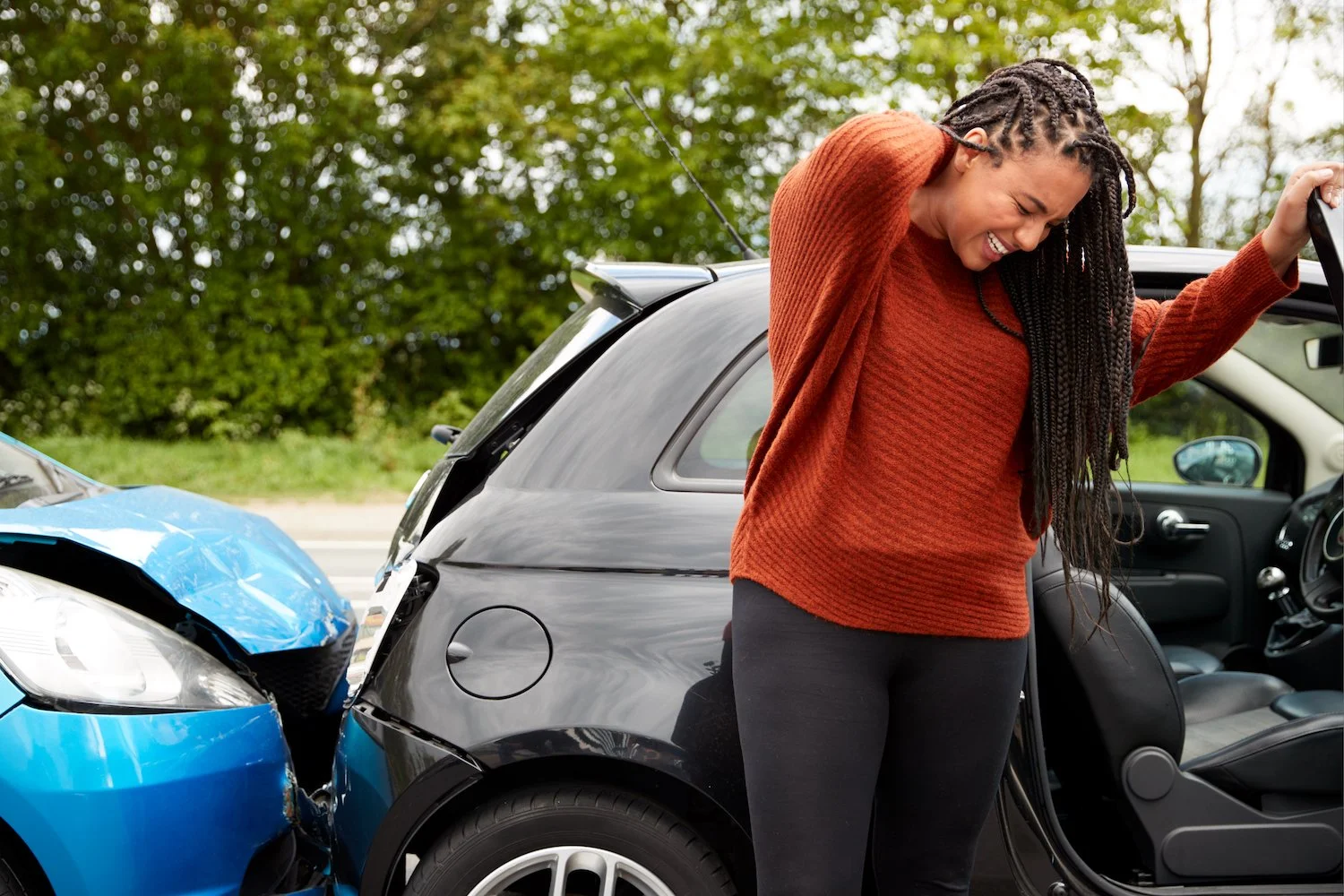 Person holding neck after auto accident with vehicle damage in background, representing injury care at Repose Wellness Center