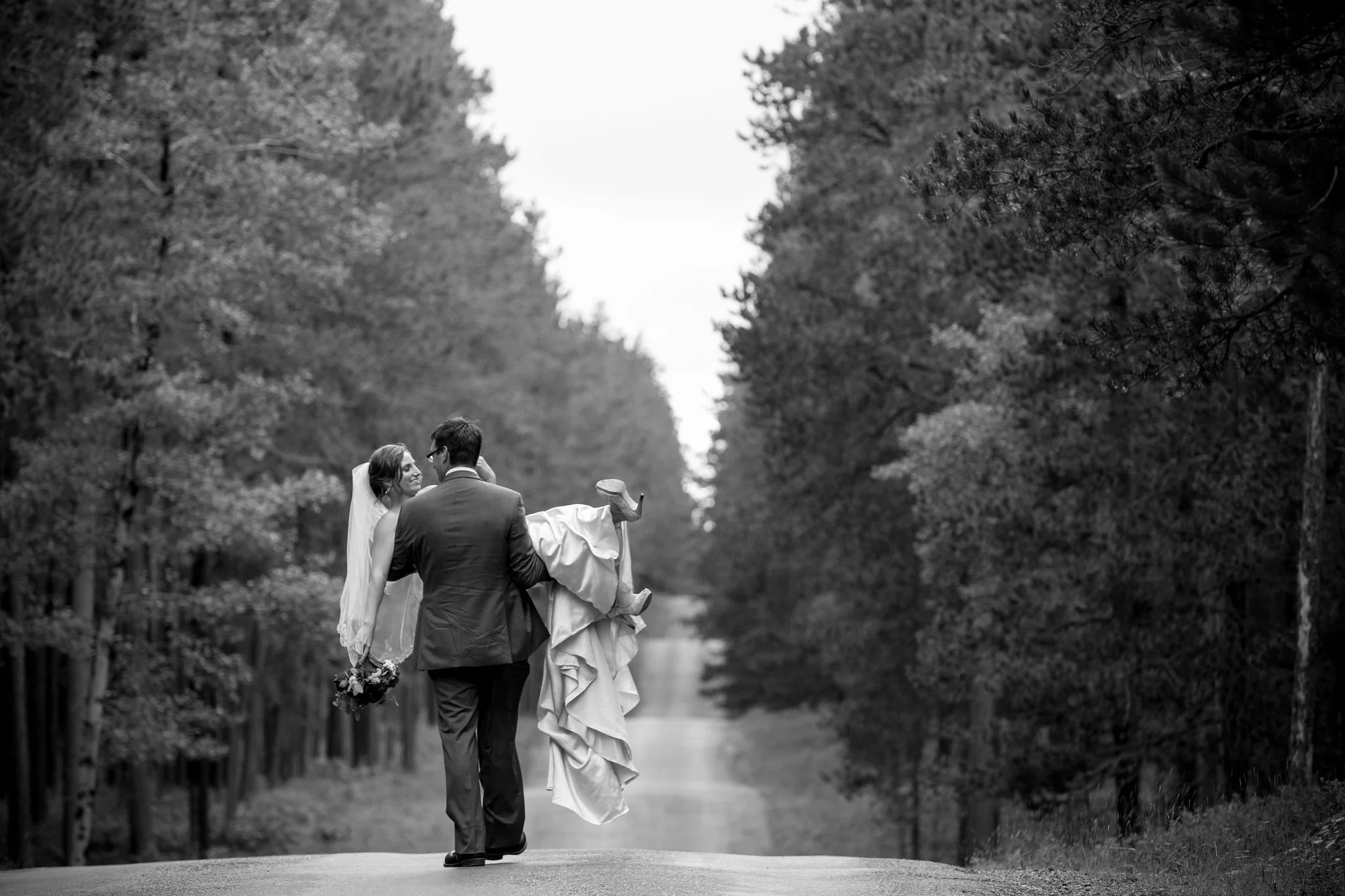 Groom carrying bride on a forest road, black and white photo