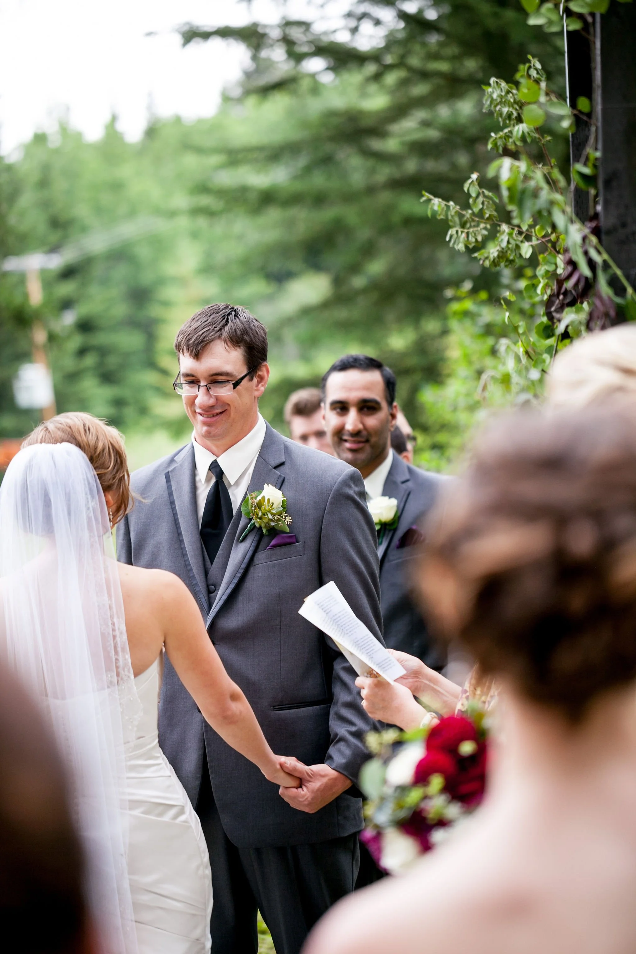 Bride and groom holding hands at an outdoor wedding ceremony with officiant and guests.