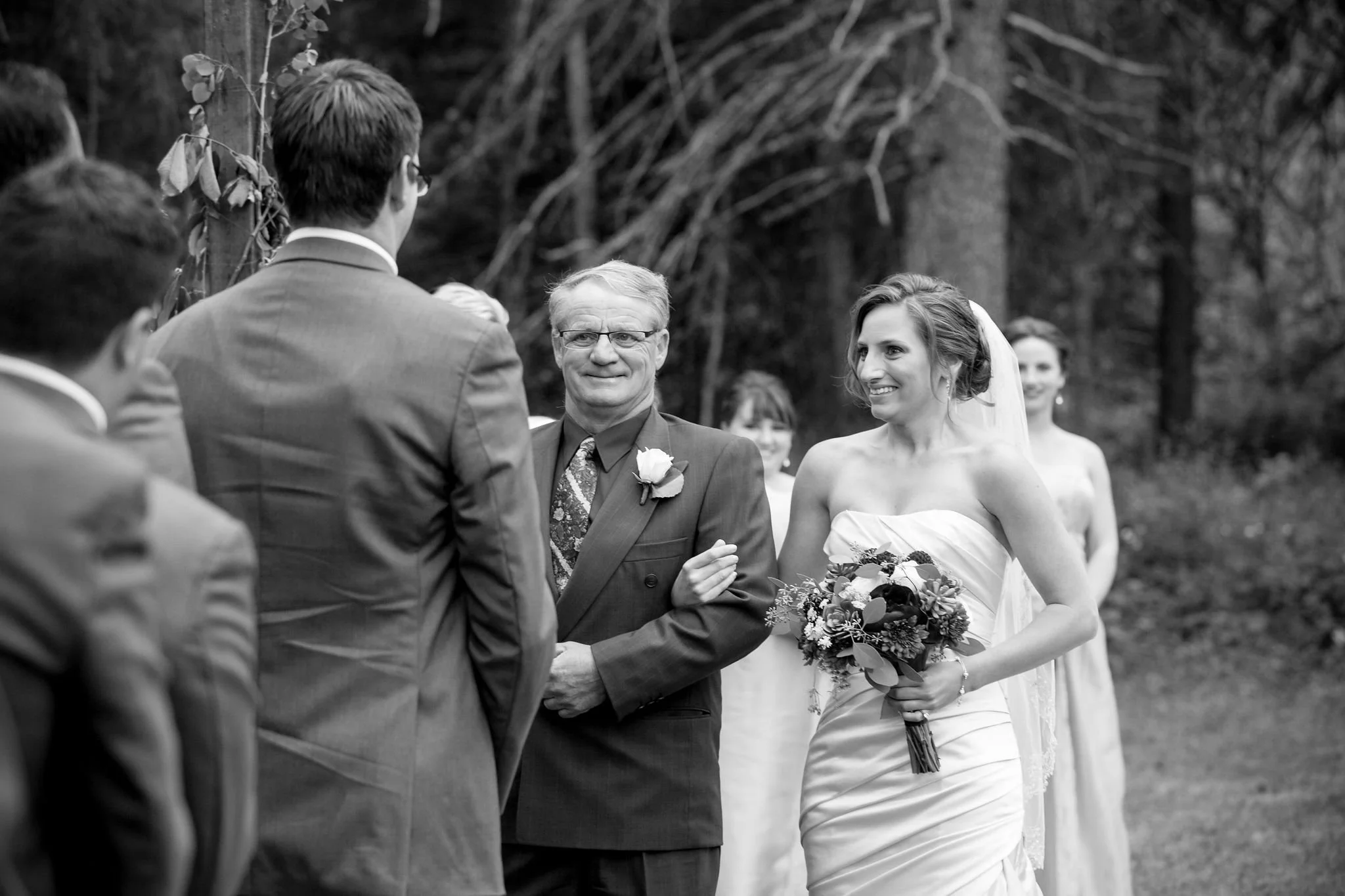 Bride in white dress walks down the aisle with her father in outdoor wedding ceremony.