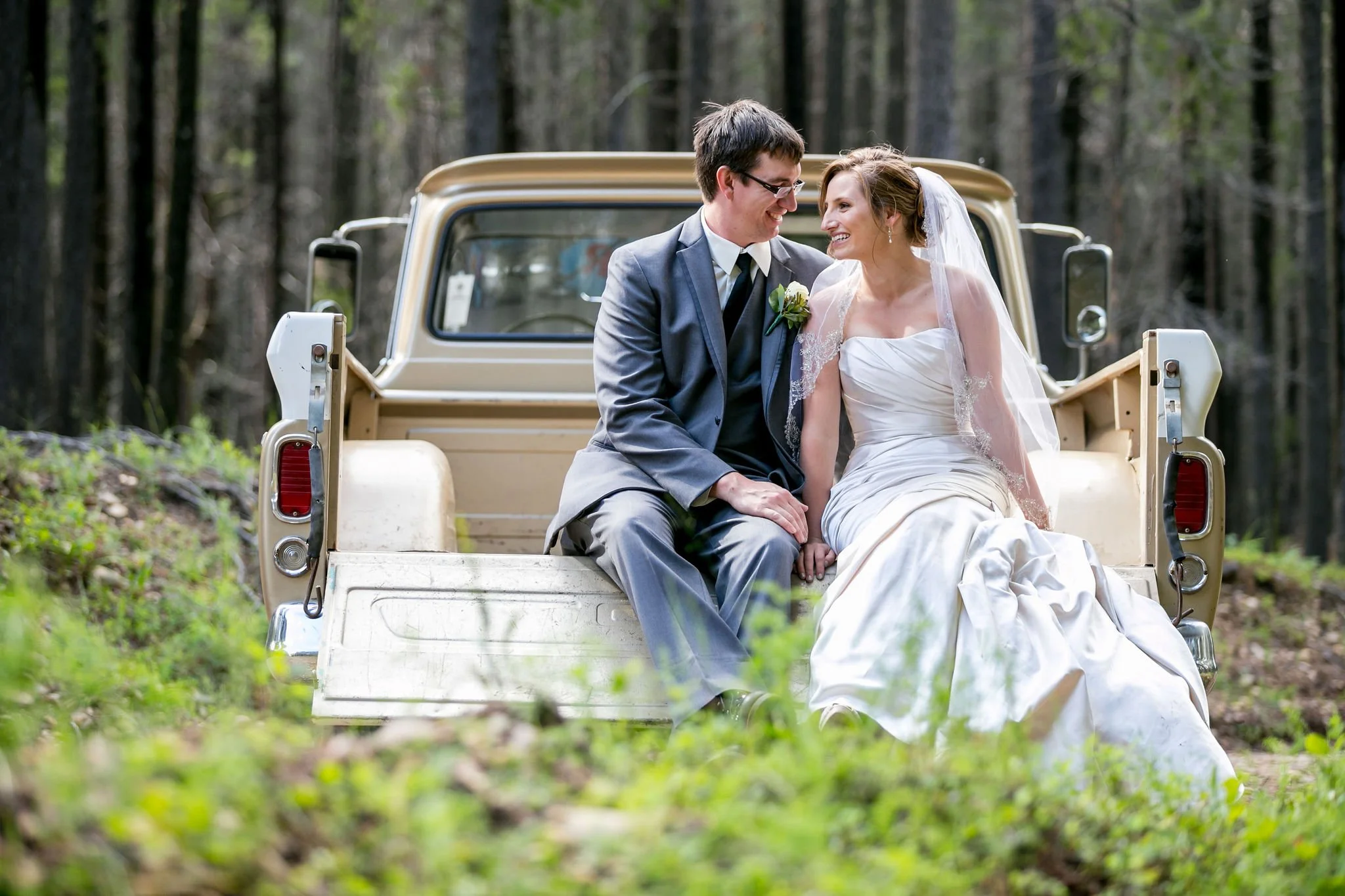A bride and groom sitting on the tailgate of a vintage truck in a forest setting.