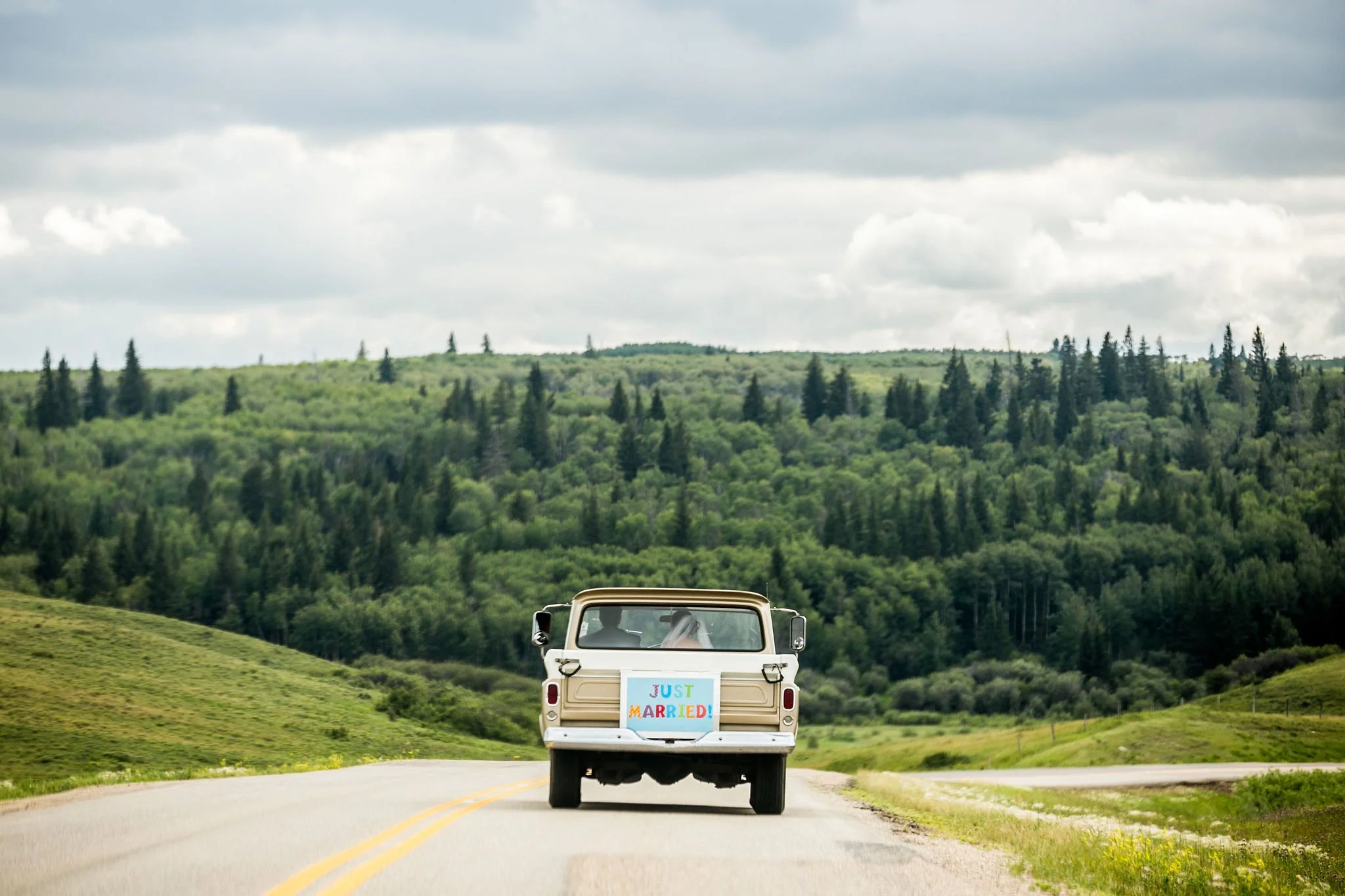 Classic car with 'Just Married' sign driving on country road