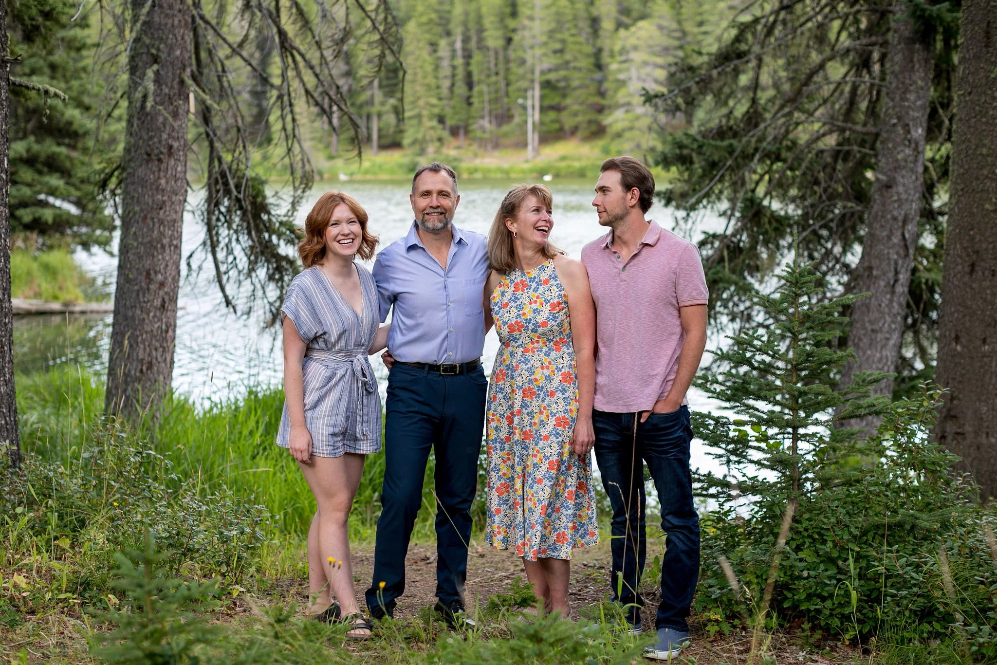 Four people standing together, smiling, in a wooded lakeside area.