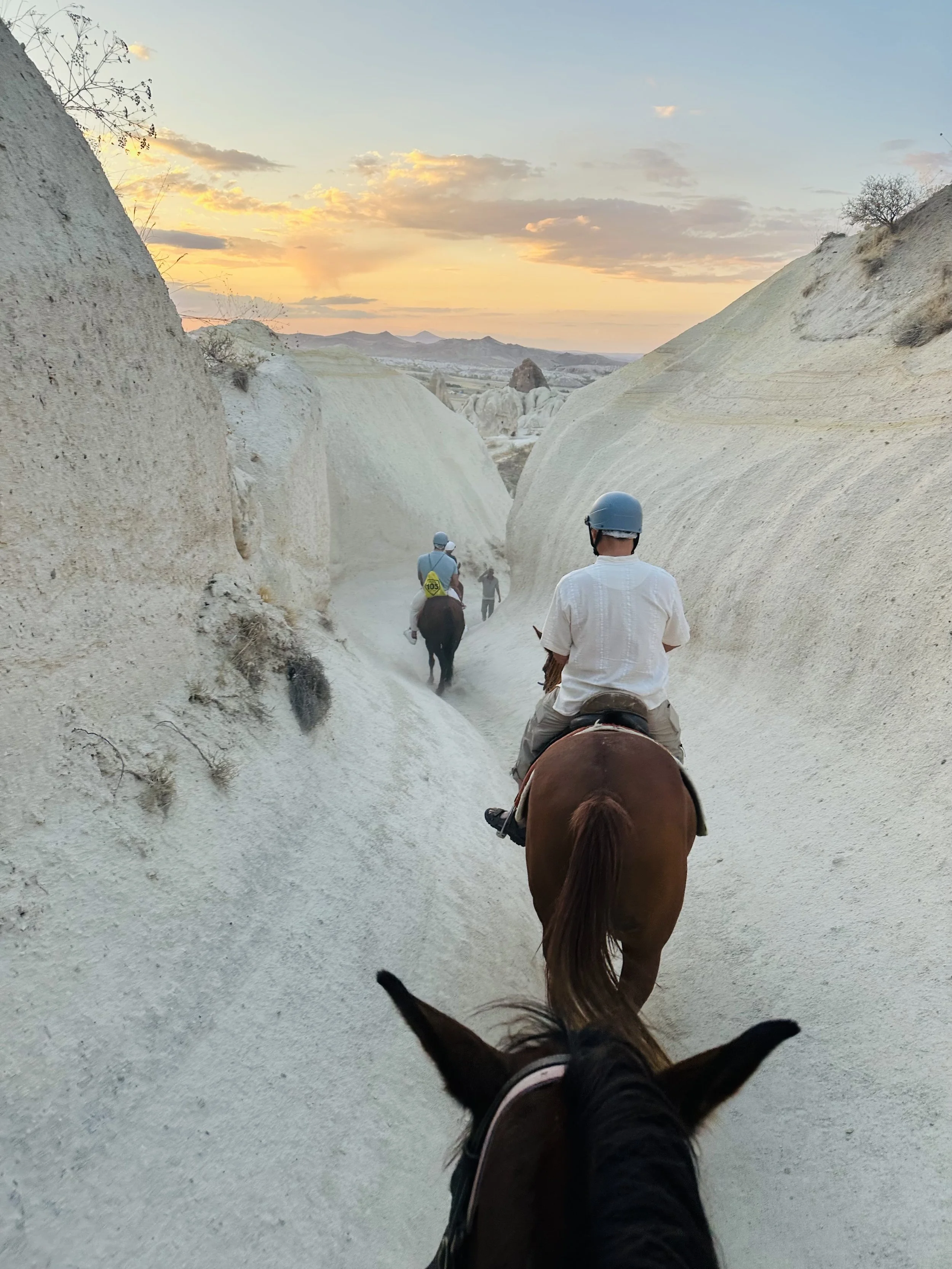People riding horses through a narrow, rocky canyon during sunset.