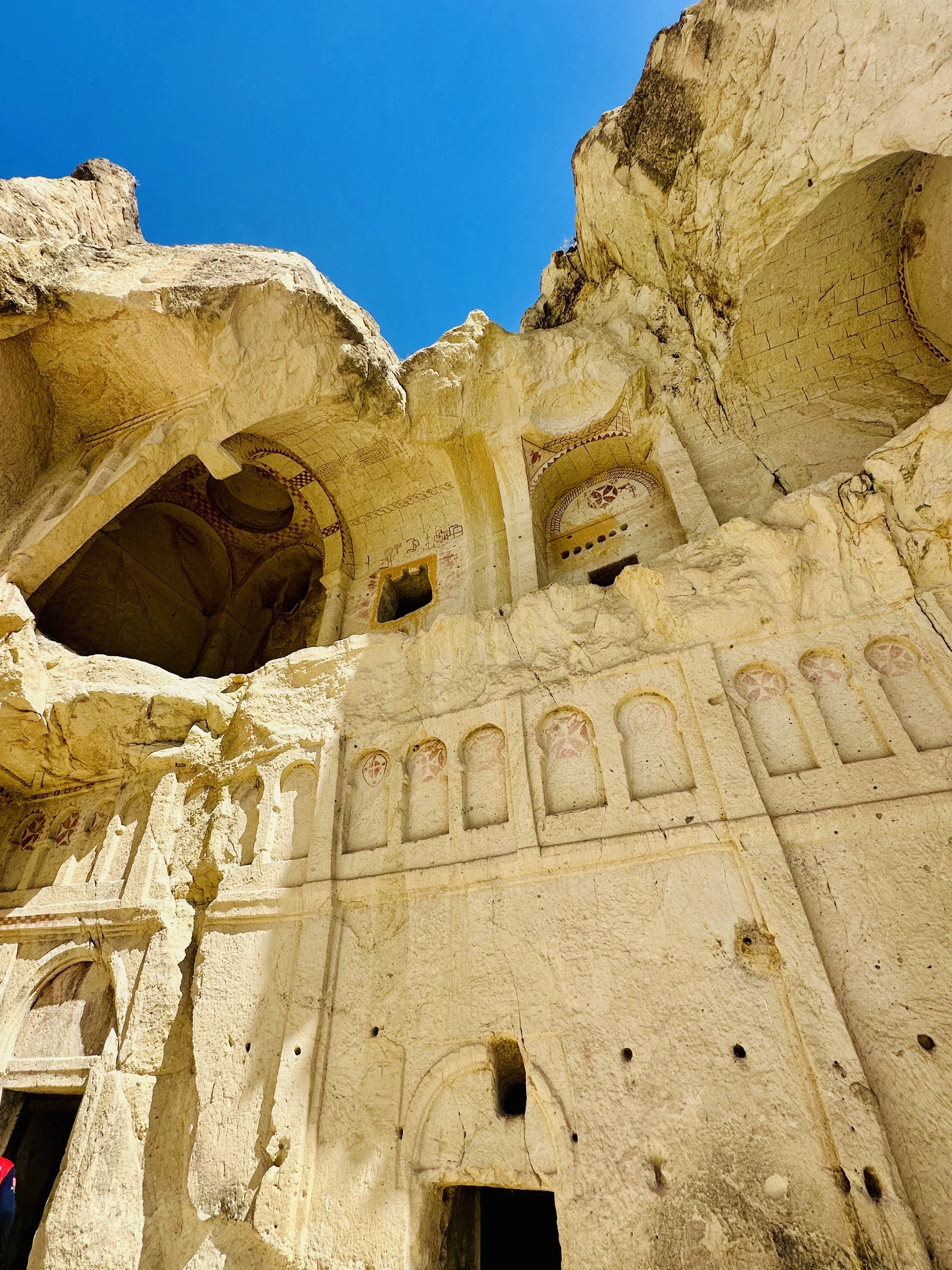 Ancient stone carved monastery or rock-cut structure with painted decorations, set against a clear blue sky.