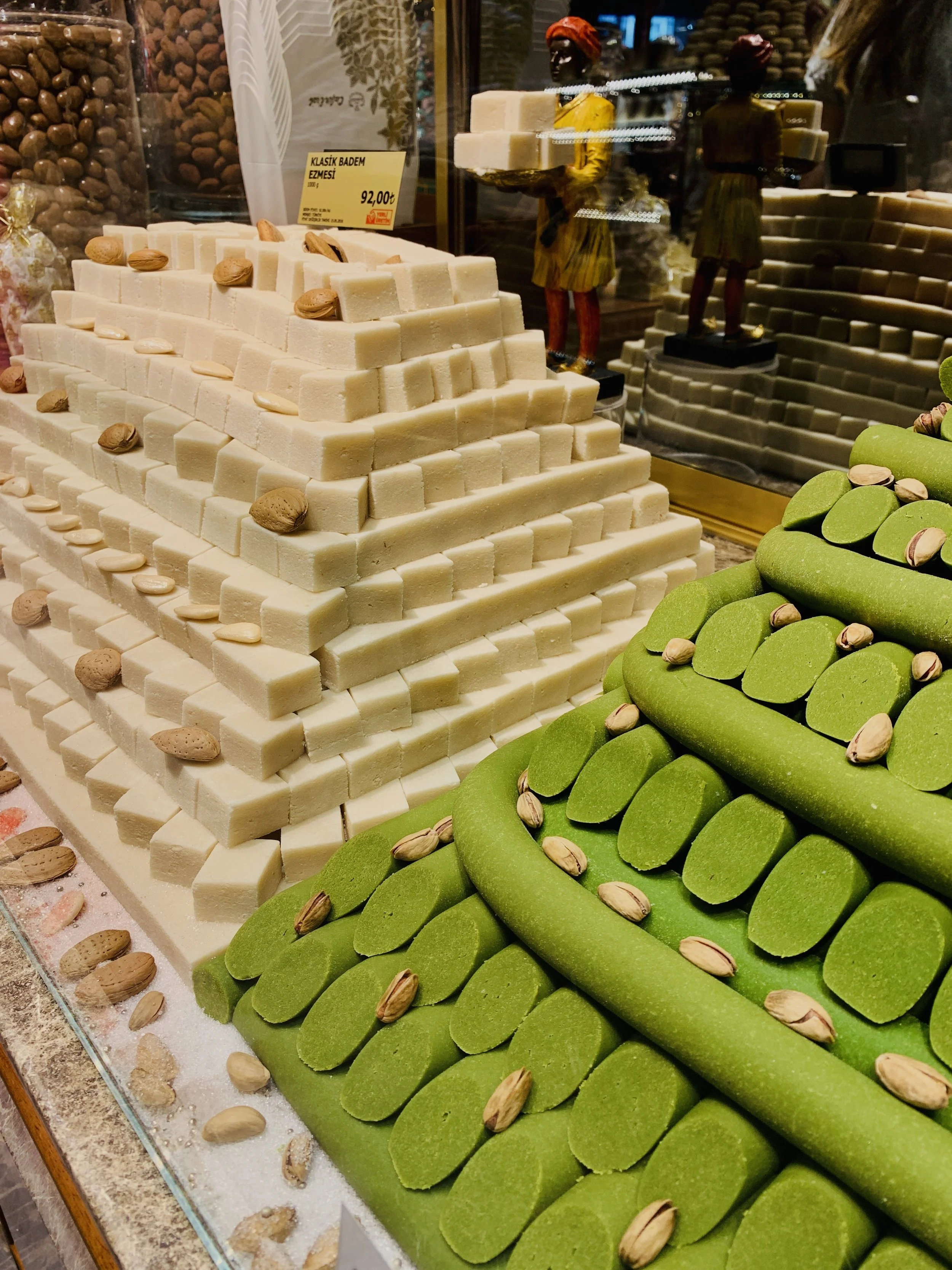 Stacks of white and green Turkish delight with almonds, displayed on a glass surface in a shop window.