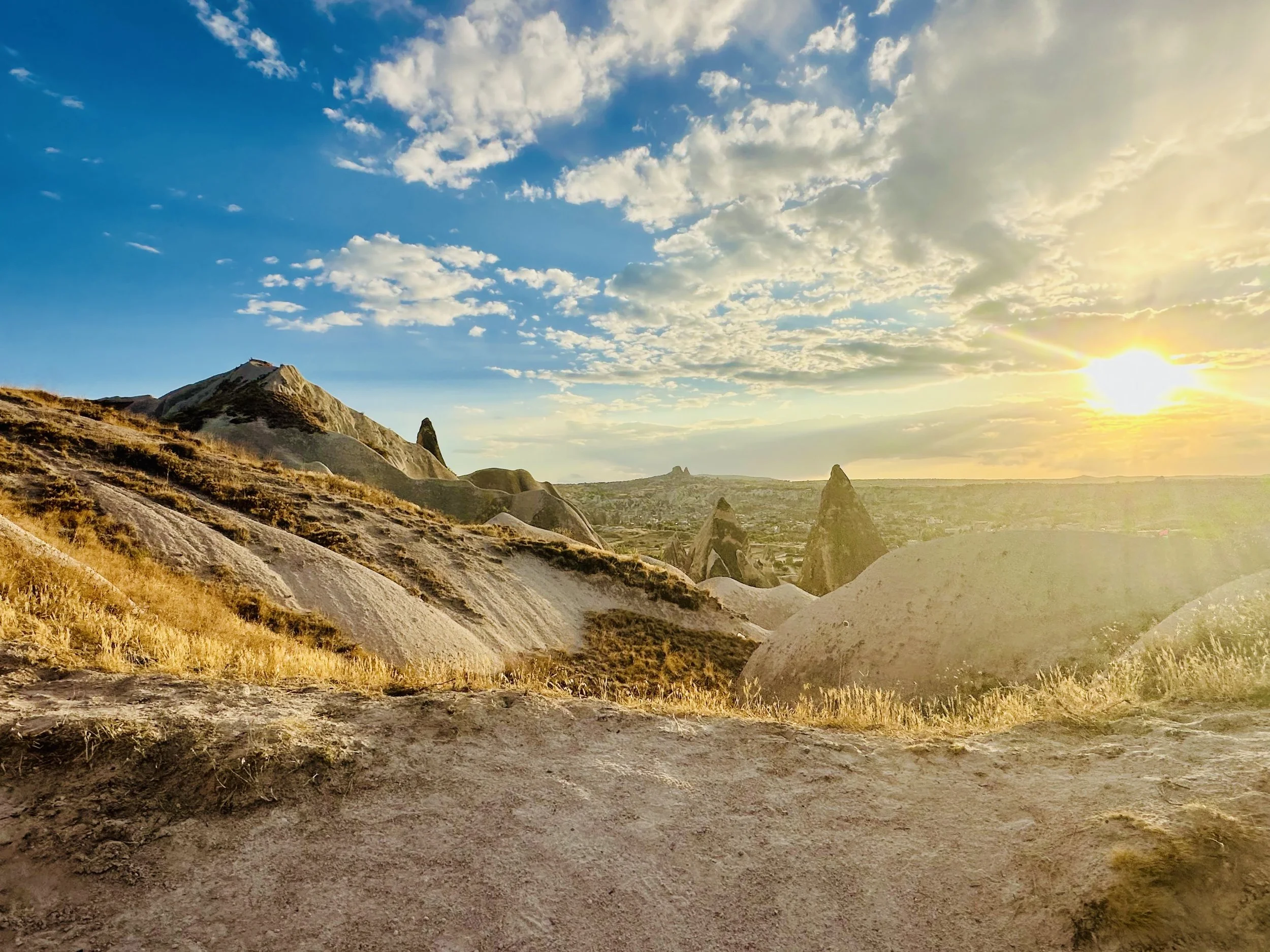 Sunset over rocky hills and unique rock formations in a semi-arid landscape with a partly cloudy sky.
