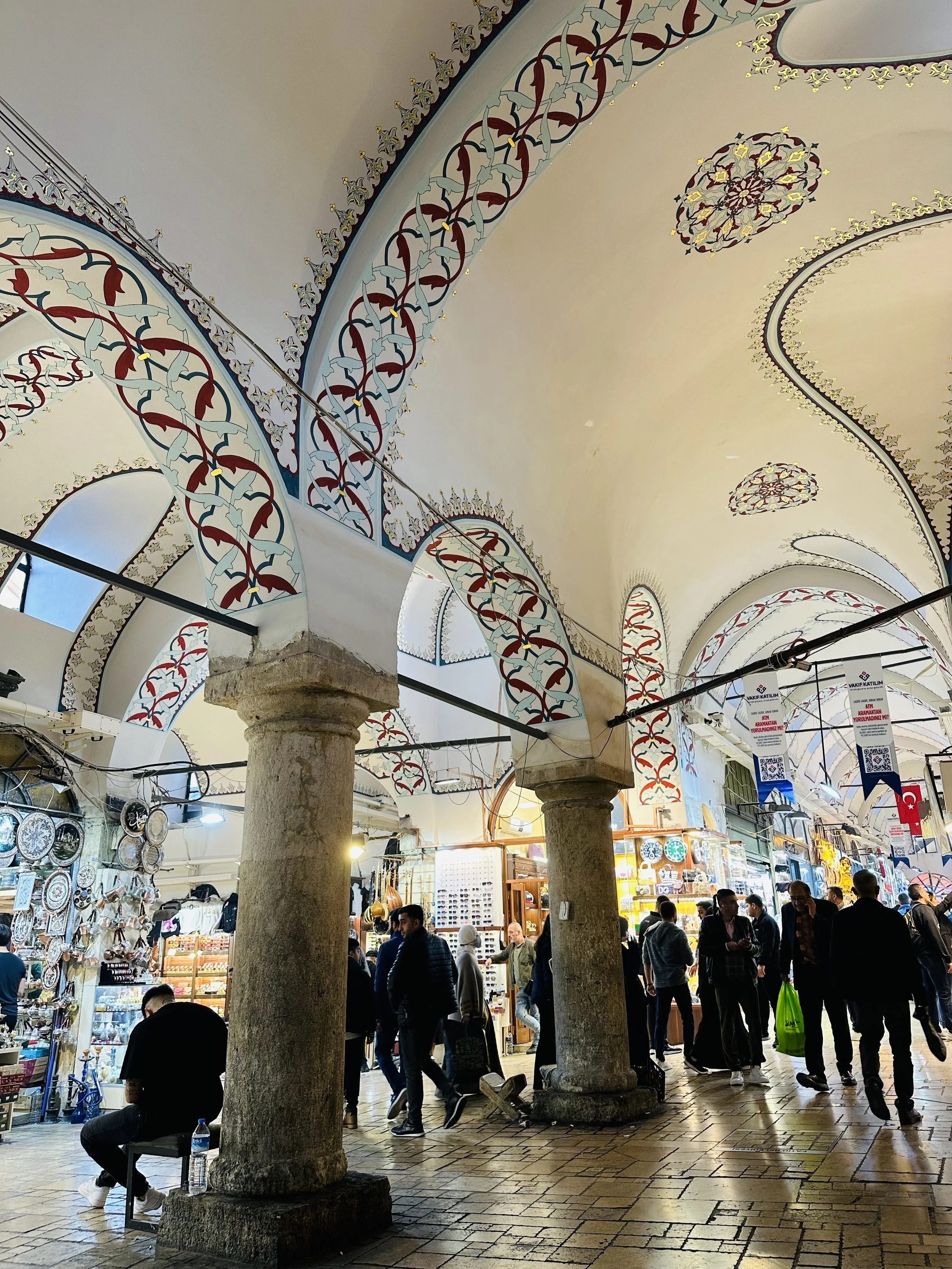 Interior of a historic marketplace with ornate painted arches and columns, bustling with shoppers browsing stores and stalls.