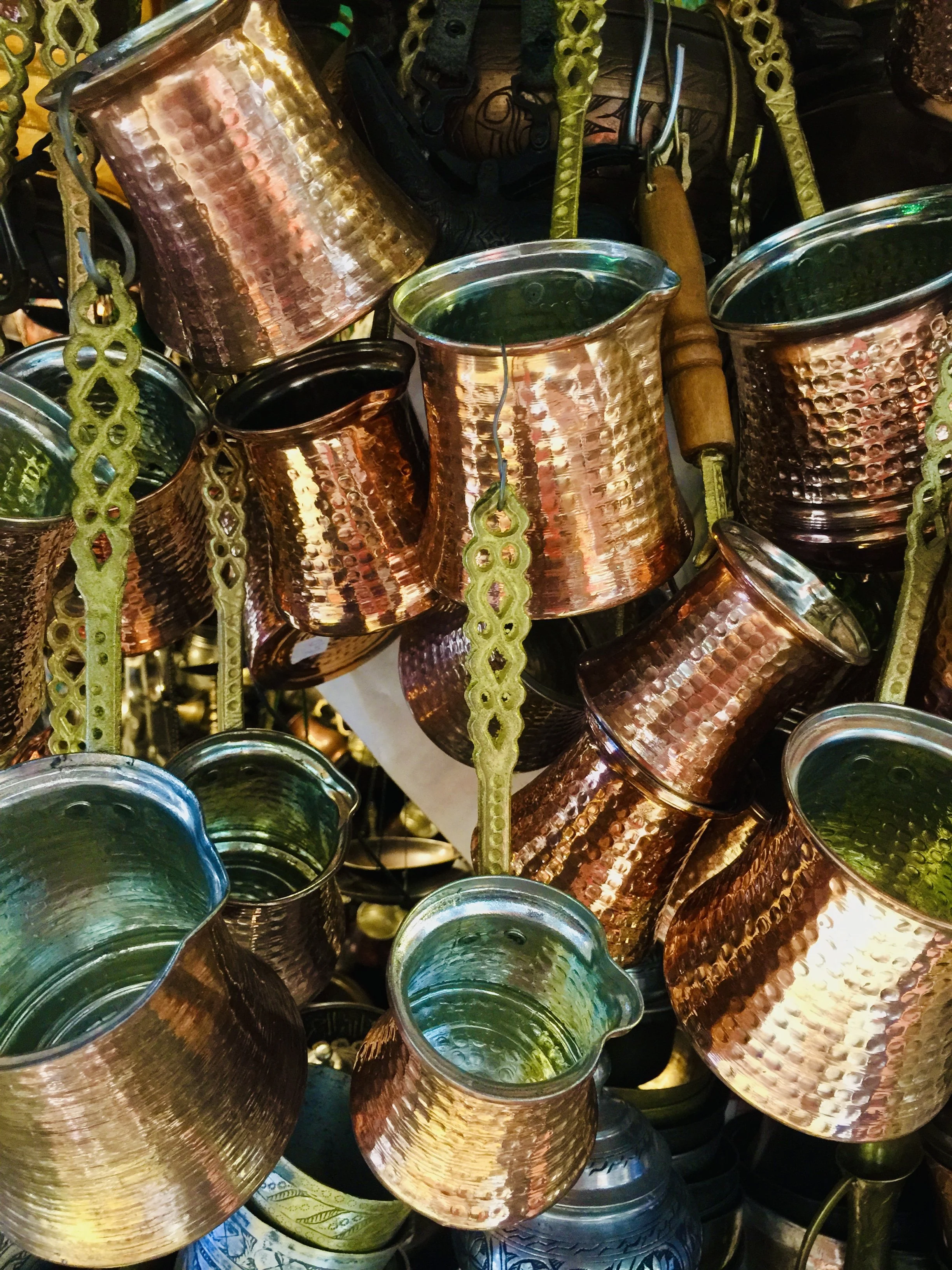 Cluster of hammered copper pots and pans with greenish interior, hanging from decorative yellow-green hooks.