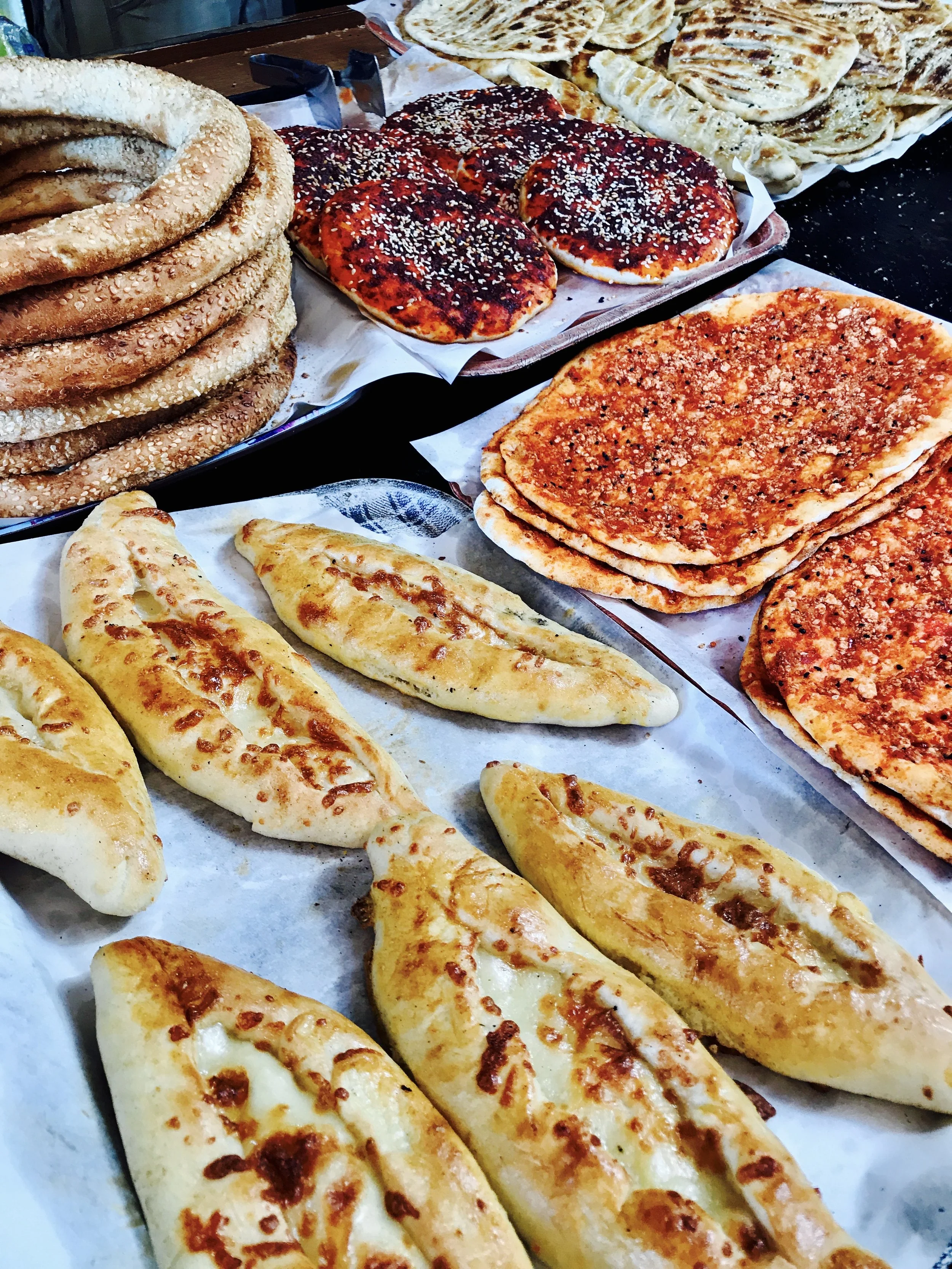 A display of various Italian foods including cheesy garlic bread, pizza slices with cheese and toppings, and stacked sesame seed bagels.