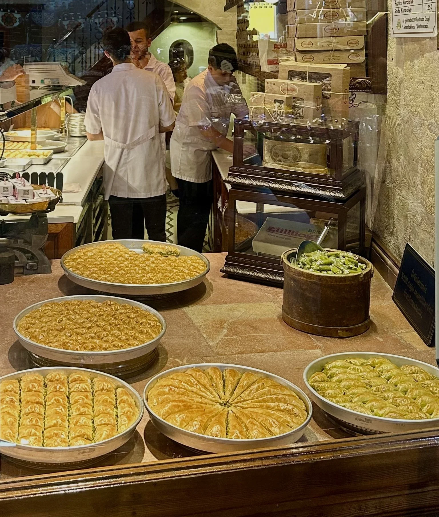 Display of various baked goods, including pies and pastries, inside a storefront with staff working behind. Reflections of the street are visible on the glass window.