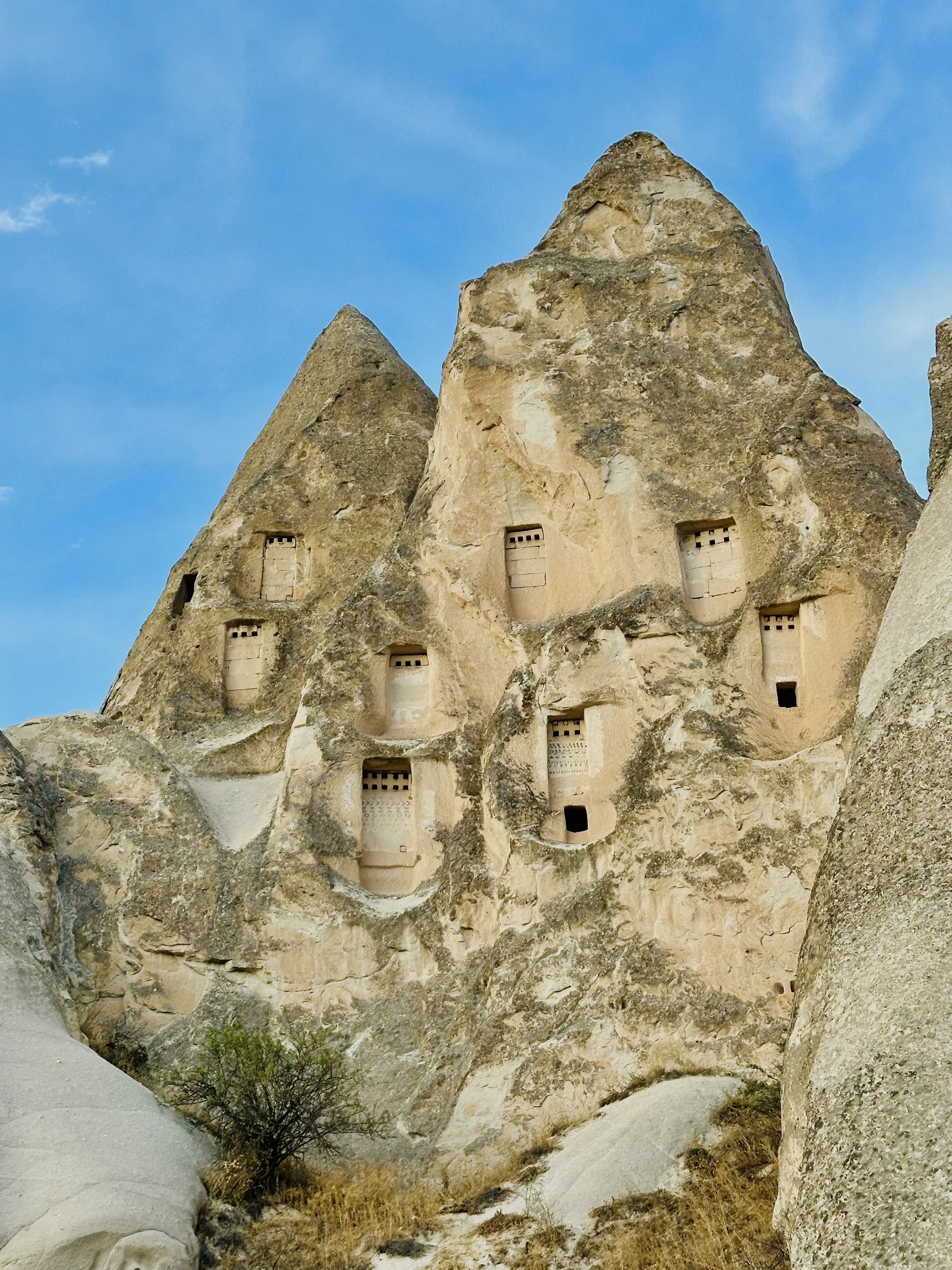 Ancient rock formations with carved cave dwellings and windows, against a blue sky.