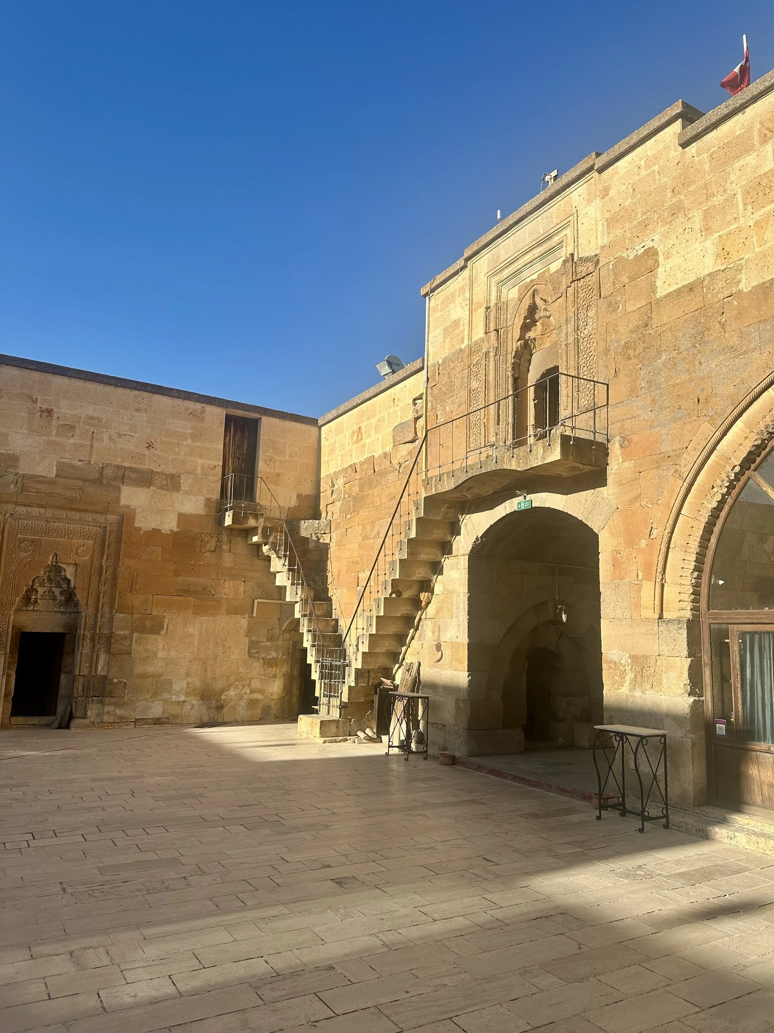 An exterior view of an old stone building with stairs, an arch, and decorative architectural details against a clear blue sky.
