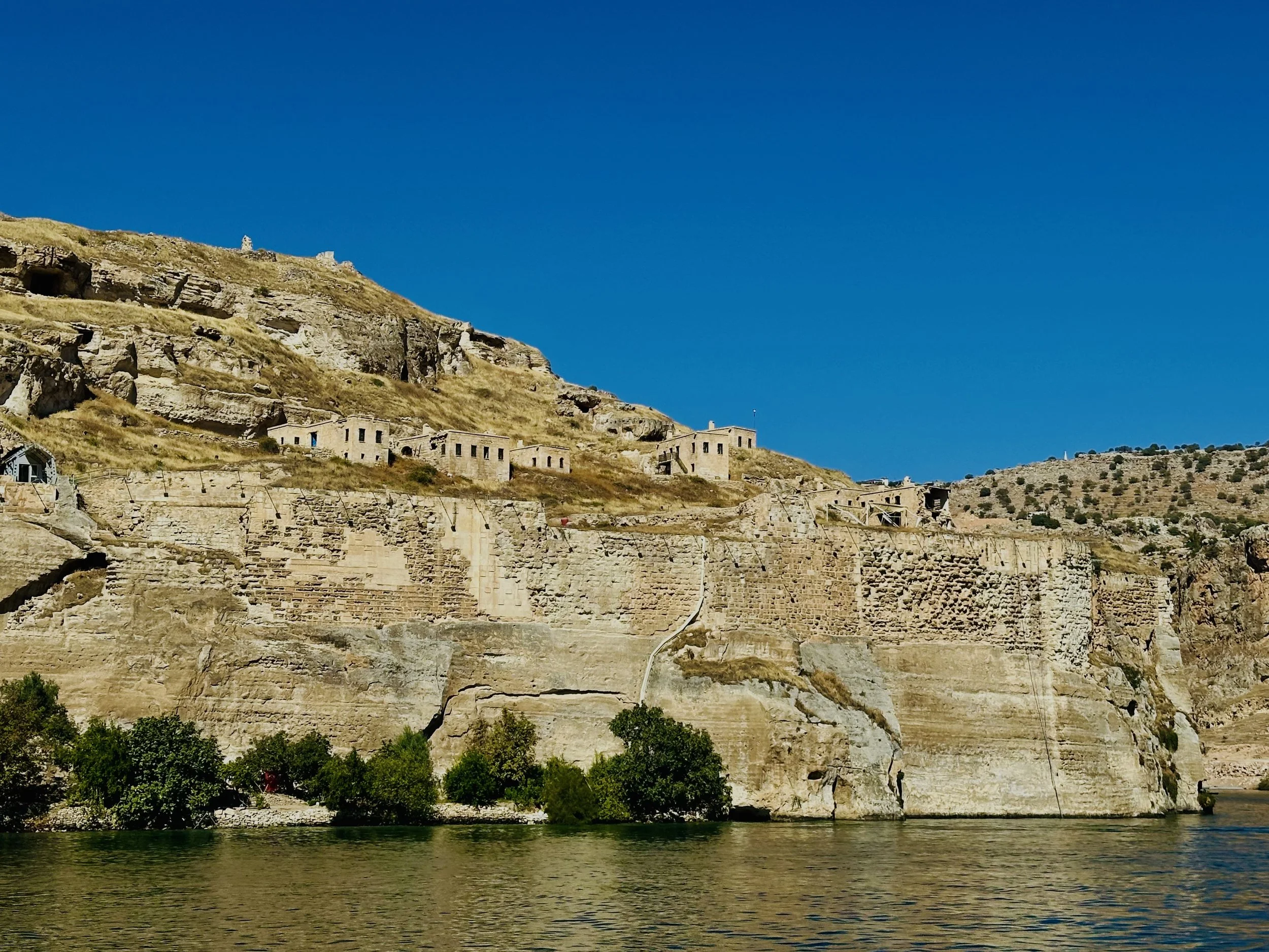 Cliffside with old stone buildings overlooking a river, under a clear blue sky.