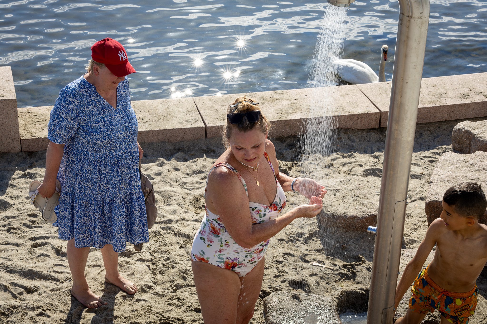 Menschen am Strand, die Wasser trinken; zwei Frauen, ein Mädchen, ein Junge, mit einem Wasserhahn am Strand.