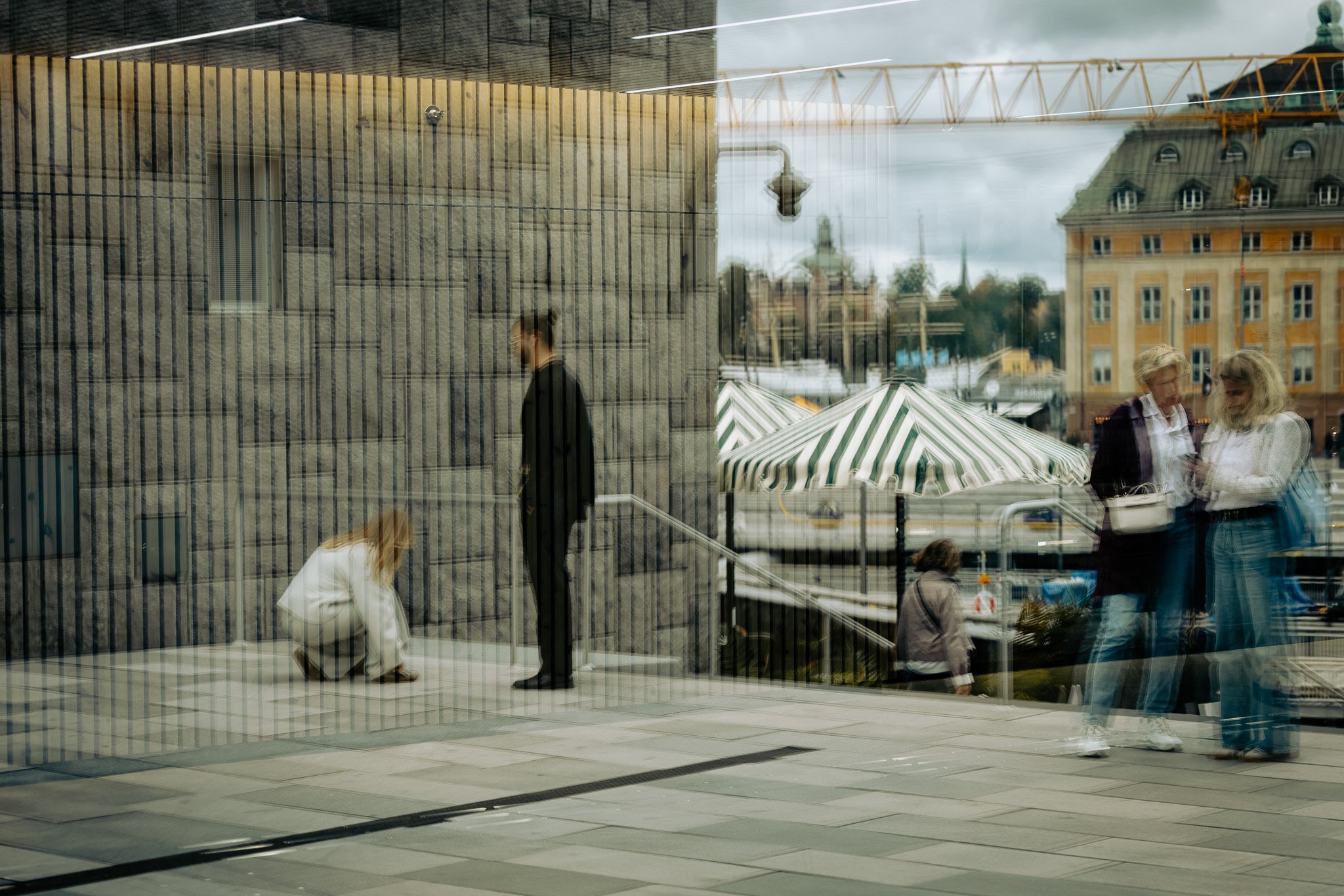 Innenansicht eines Gebäudes mit Blick nach draußen auf die Stadt und Regentage, Menschen im Gespräch, spiegelnde Glasflächen
