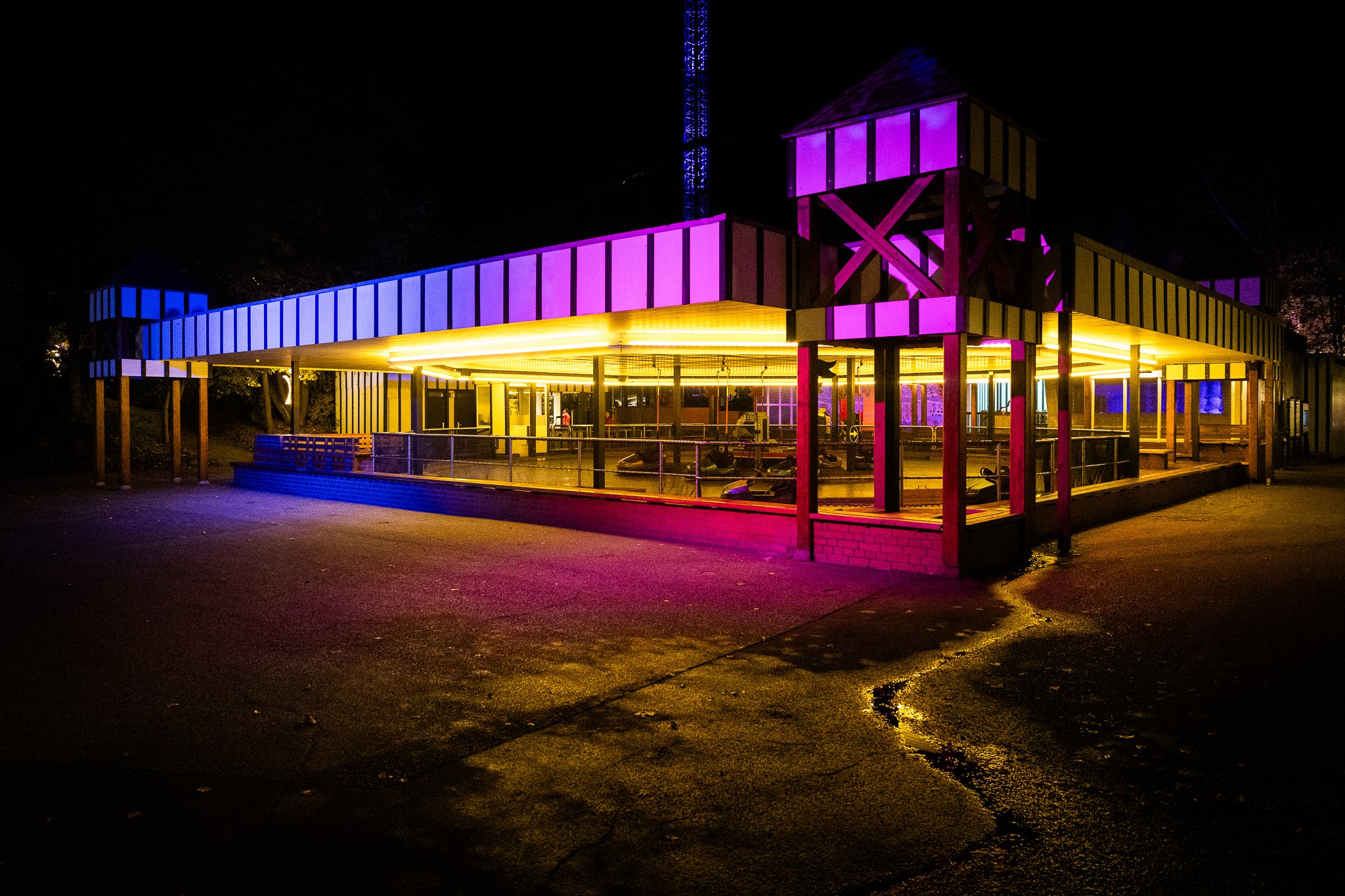 Ein Karussell bei Nacht, beleuchtet mit bunten Lichtern in Blau, Rosa und Gelb.