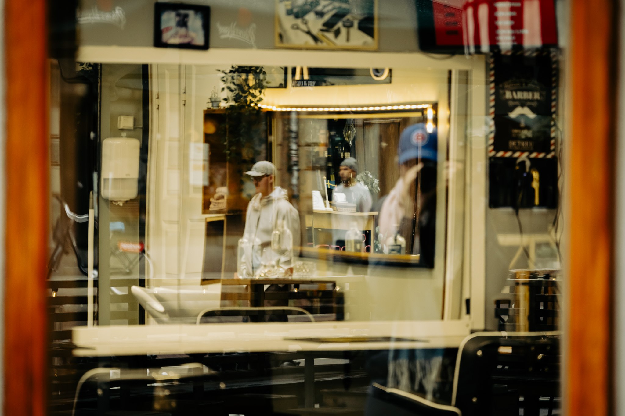 Spiegelbild eines Cafés oder Restaurants in einer Fensterfront mit mehreren Gästen, Blumen und Dekorationen im Innenraum, vermutlich in einer Stadt.