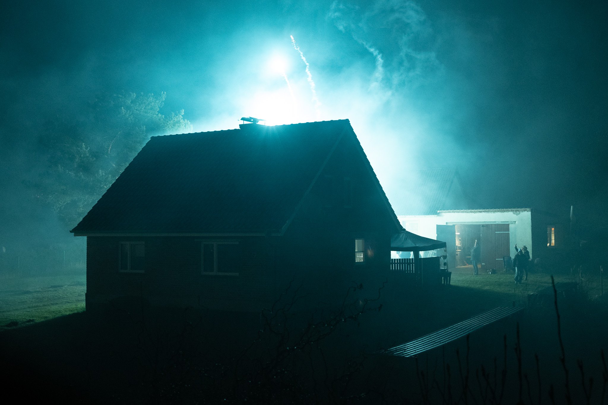 Ein Haus bei Nacht mit einem hell erleuchteten Himmel und Figuren auf der Wiese neben dem Haus.