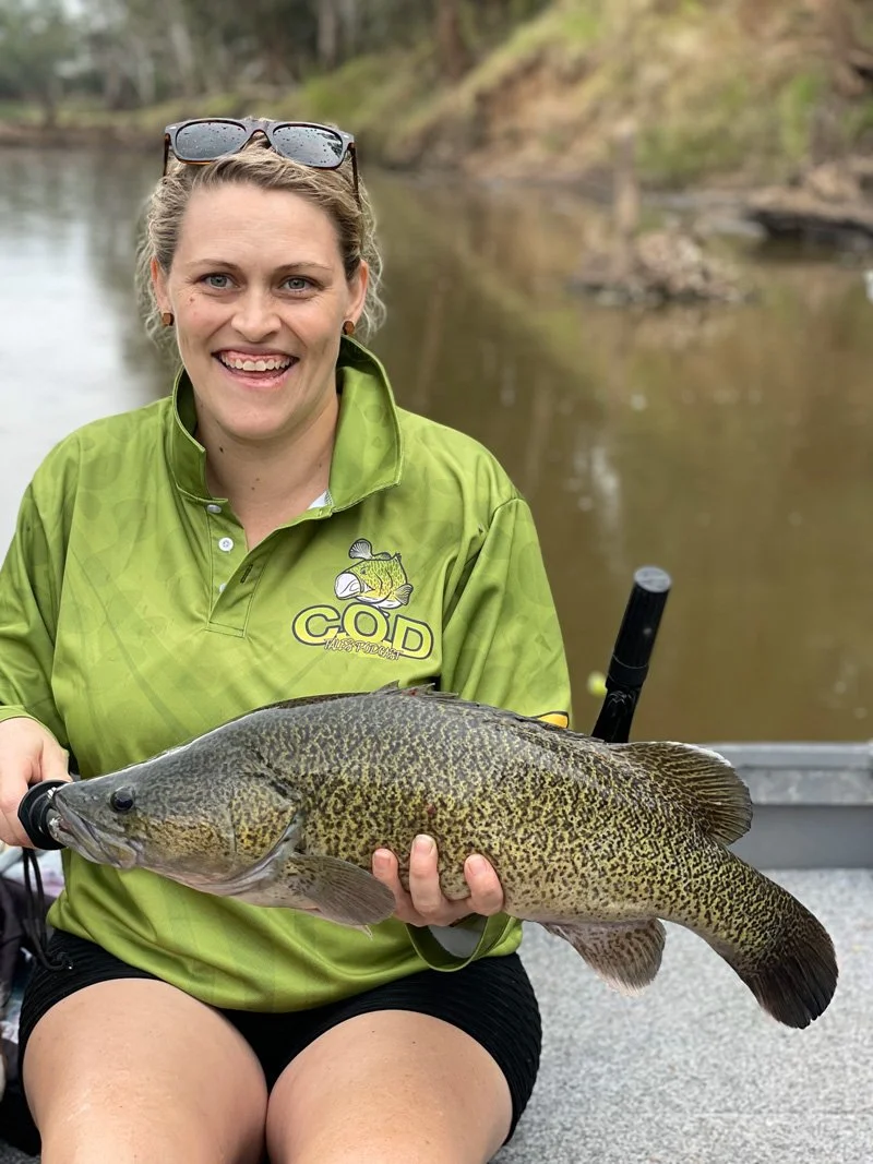 lady holding up a cod wearing her COD Tales fishing shirt