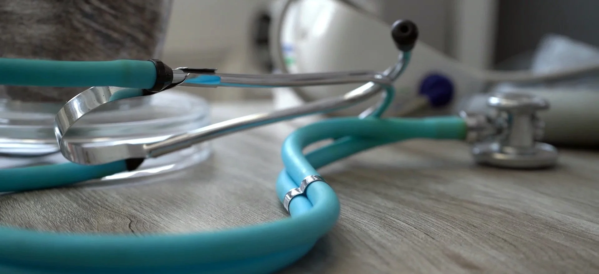 A stethoscope with teal tubing lying on a wooden surface.