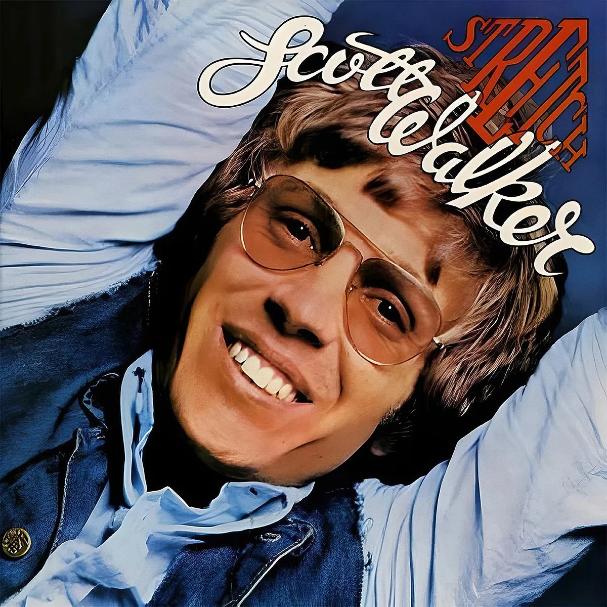 A person with short hair, wearing sunglasses, smiling, lying on a bed with white pillows, and wearing a denim vest over a white shirt. The text 'Strickly Jassy & Telewber' is written on the image.