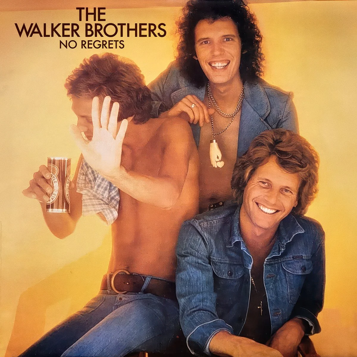 Album cover of The Walker Brothers' 'No Regrets' featuring all three smiling with long hair, Scott is shirtless drinking a can of beer, with a yellow background.