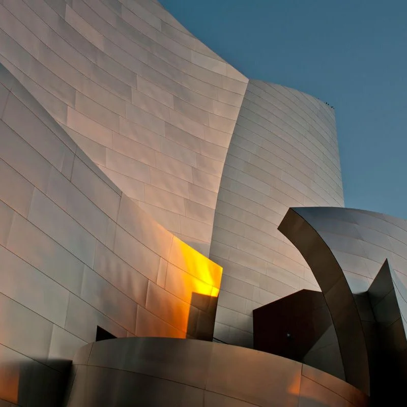 Close-up view of modern, abstract building with curved metallic surfaces reflecting sunset colors.