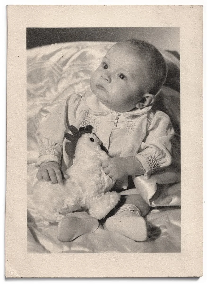 A black and white photograph of a young Scott Walker, aged about 10 months, sitting on a bed, holding a stuffed animal toy.