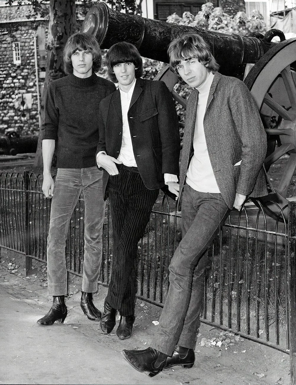The Walker Brothers standing outdoors in front of a cannon, cityscape background, black and white photograph circa 1965.