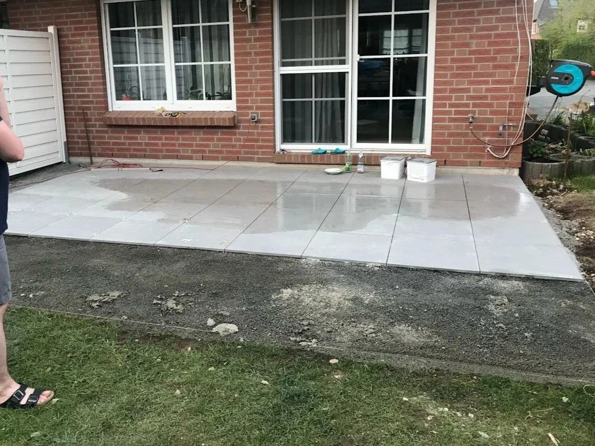 Neue geblockte Steinplatte vor einem Haus, mit Bauarbeiten und Werkzeugen im Garten.