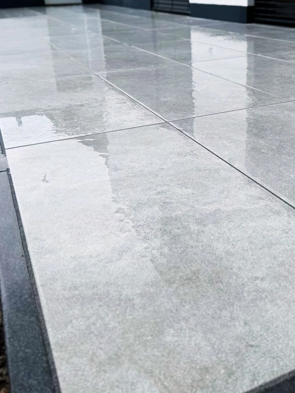 Nass glänzende Fliesen auf einem Boden, die das Licht reflektieren.