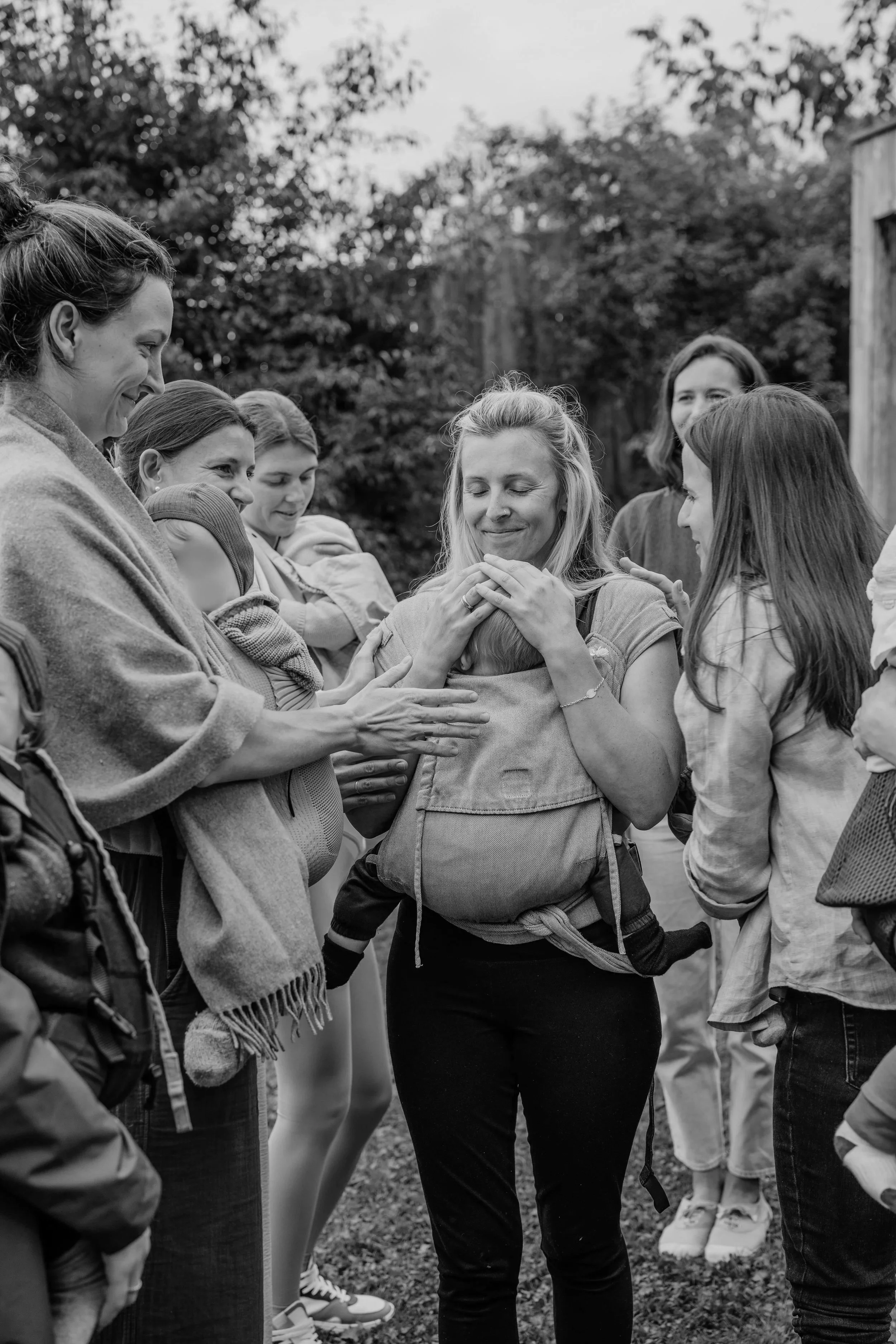 Eine Mutter trägt ihr Kind in der Trage und wird von anderen Frauen mit Kindern umringt