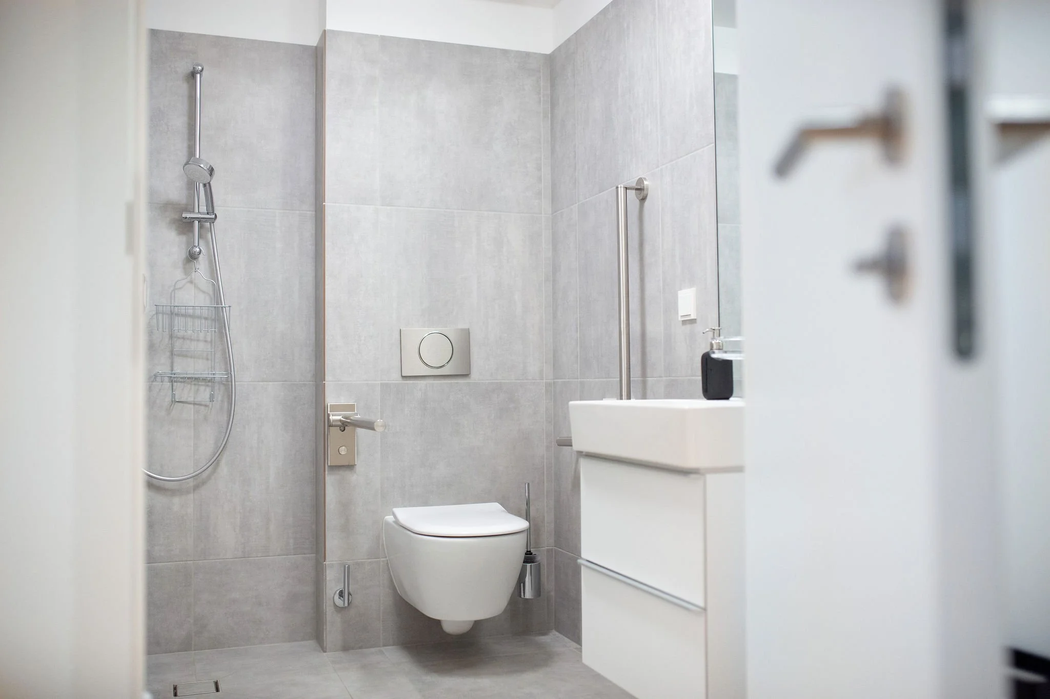 Modernes barrierefreies Badezimmer mit Dusche, Toilette und Waschbecken, Rollstuhlzugang, graue Fliesen.