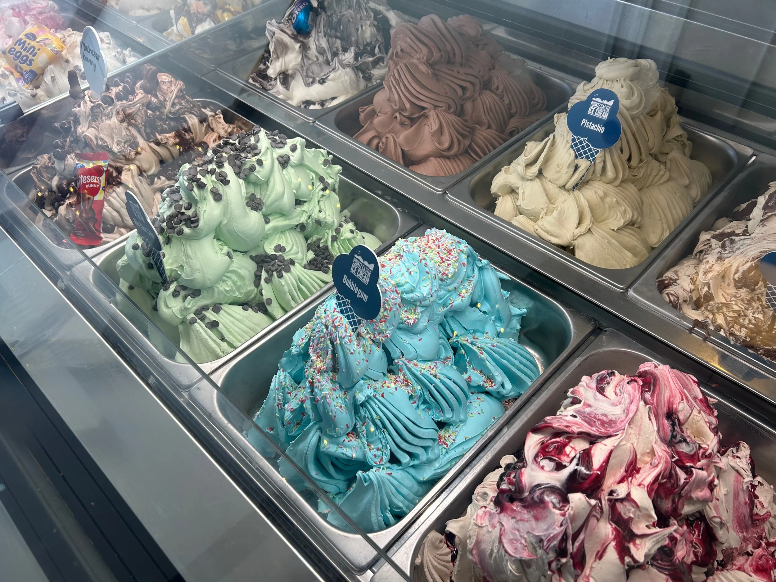 Assorted flavors of gelato in a display case, including chocolate, pistachio, bubblegum, and berry swirl.