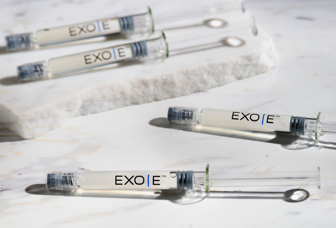 Multiple syringes labeled "EXO|E" lying on a white surface with some sitting on a marble slab. HER Aesthetics in Oswego, IL